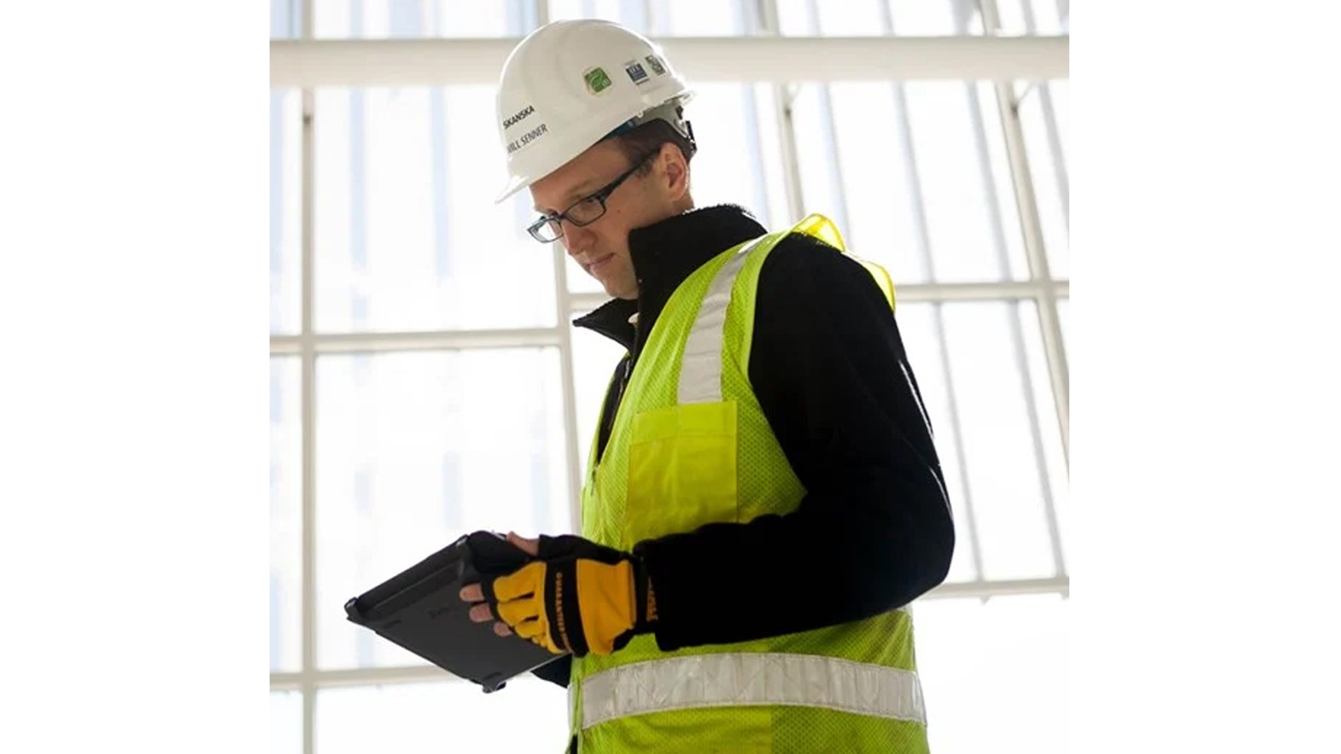 Construction worker wearing a helmet and safety vest using a tablet indoors.