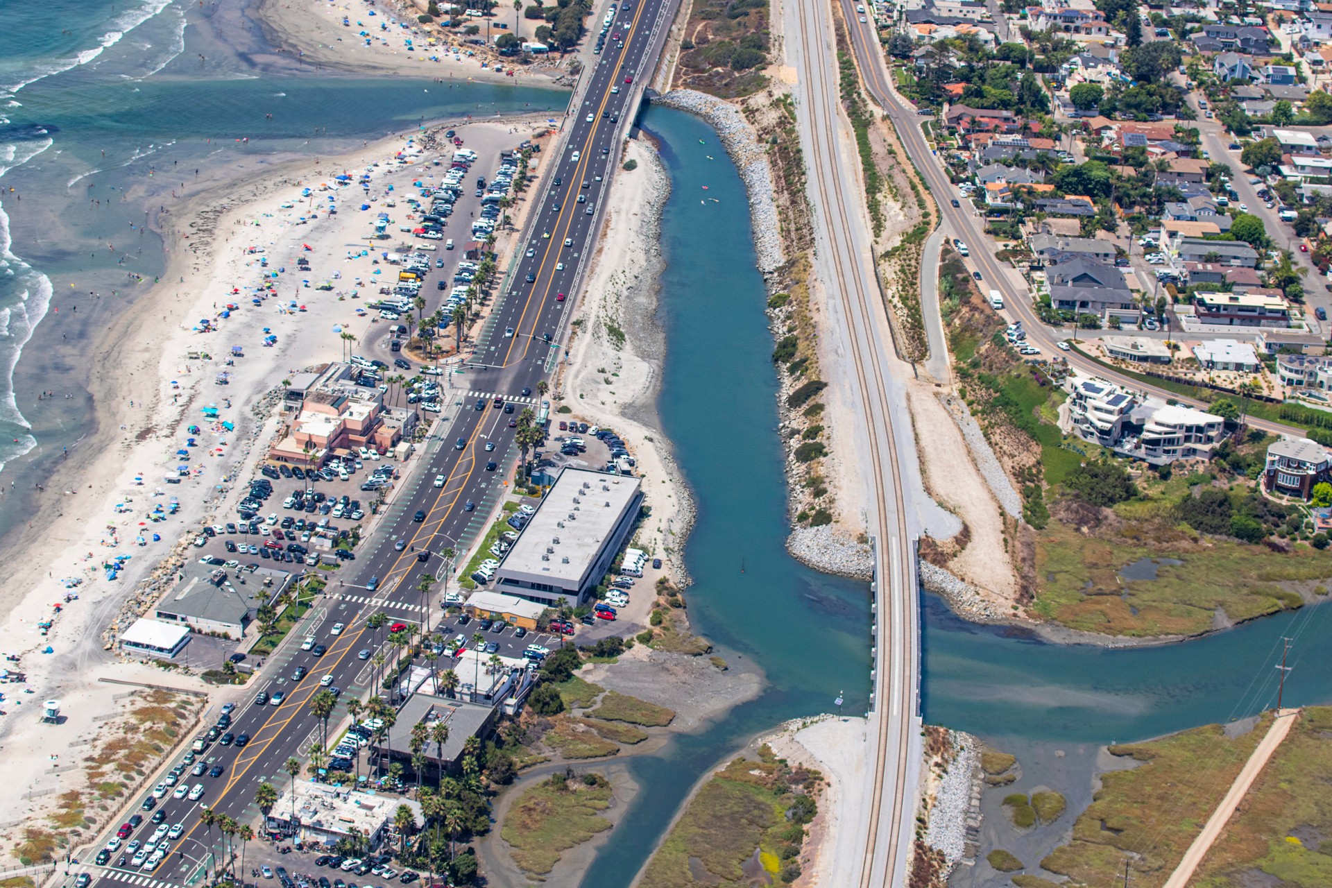 Aerial view of coastal highway and beach with ocean waves Aerial view of coastal highway with beach, ocean, and residential area beside waterway.