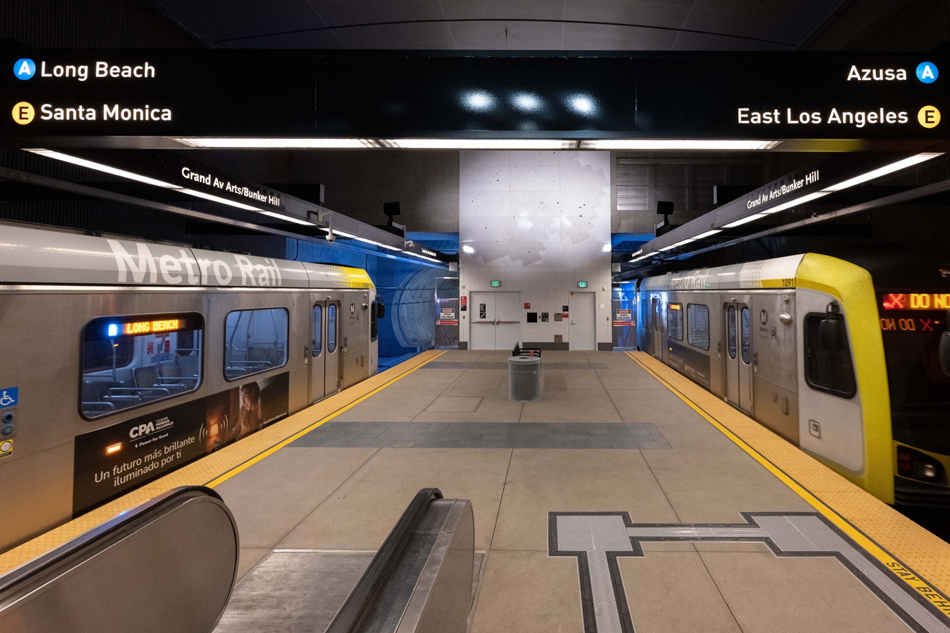 Metro Rail station platform with two trains and directional signs for Long Beach and Azusa.