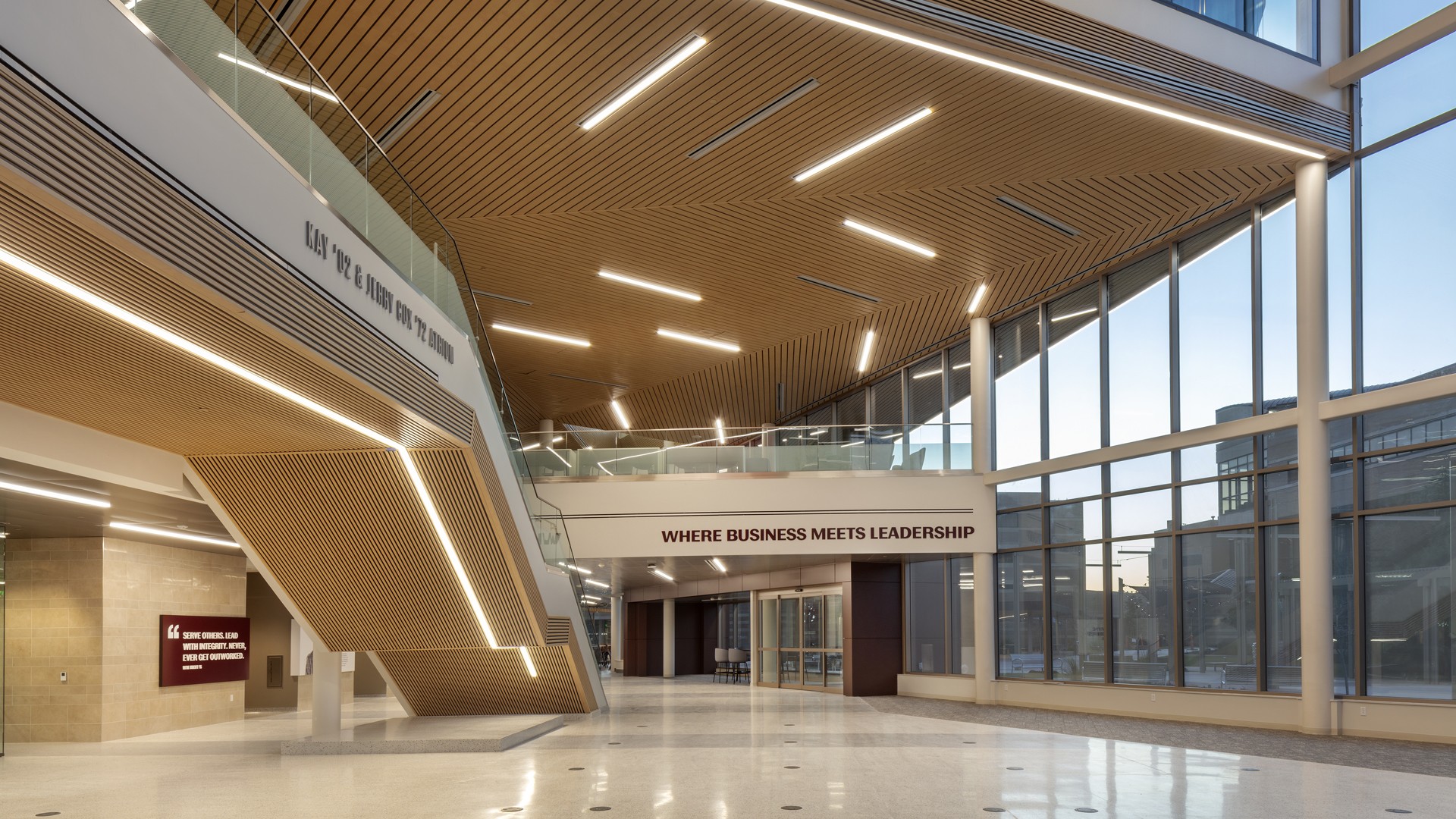 Modern spacious office lobby with large windows, wooden ceiling, and leadership quote.