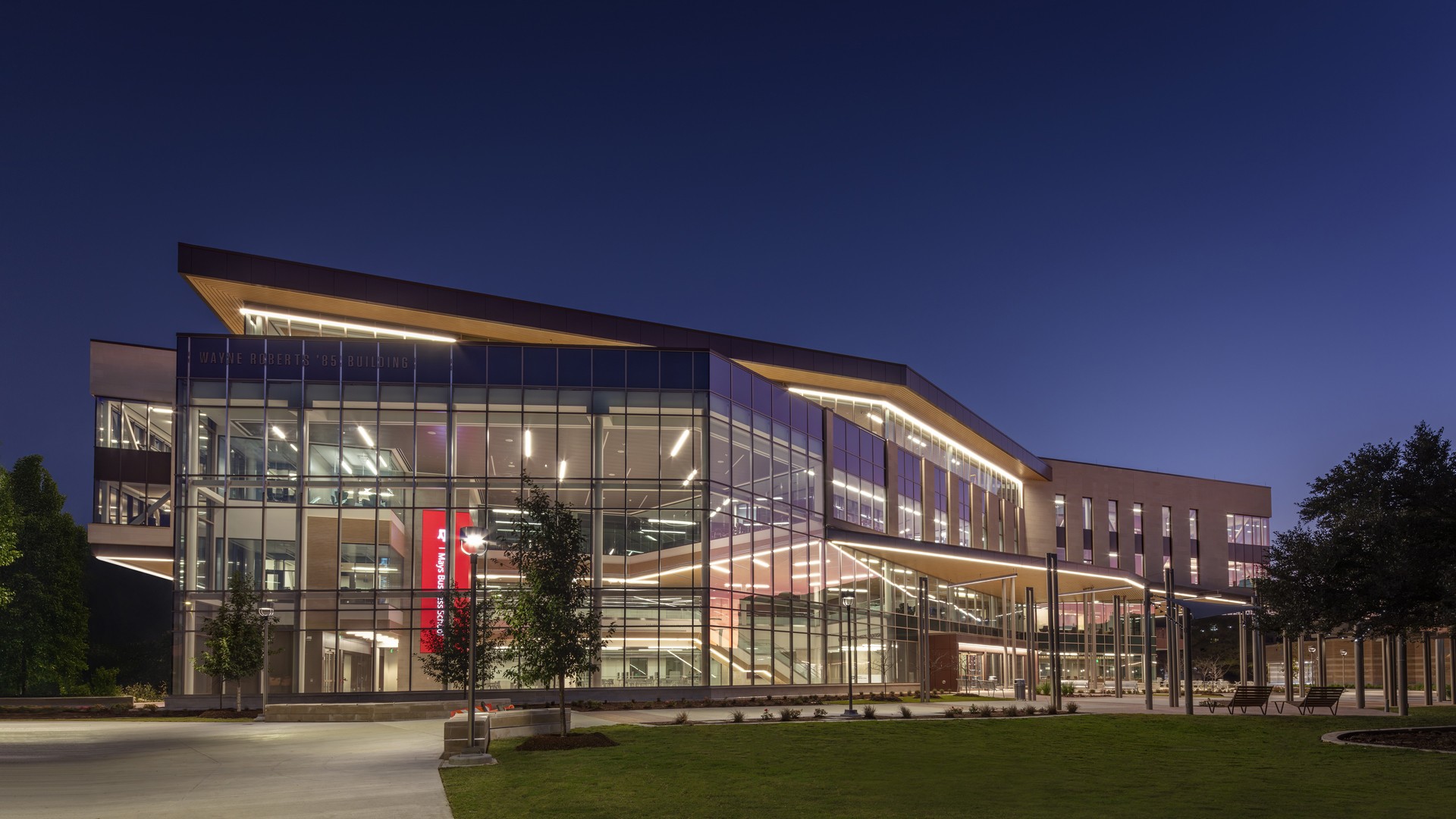 Modern glass-fronted building illuminated at dusk with a clear evening sky background.