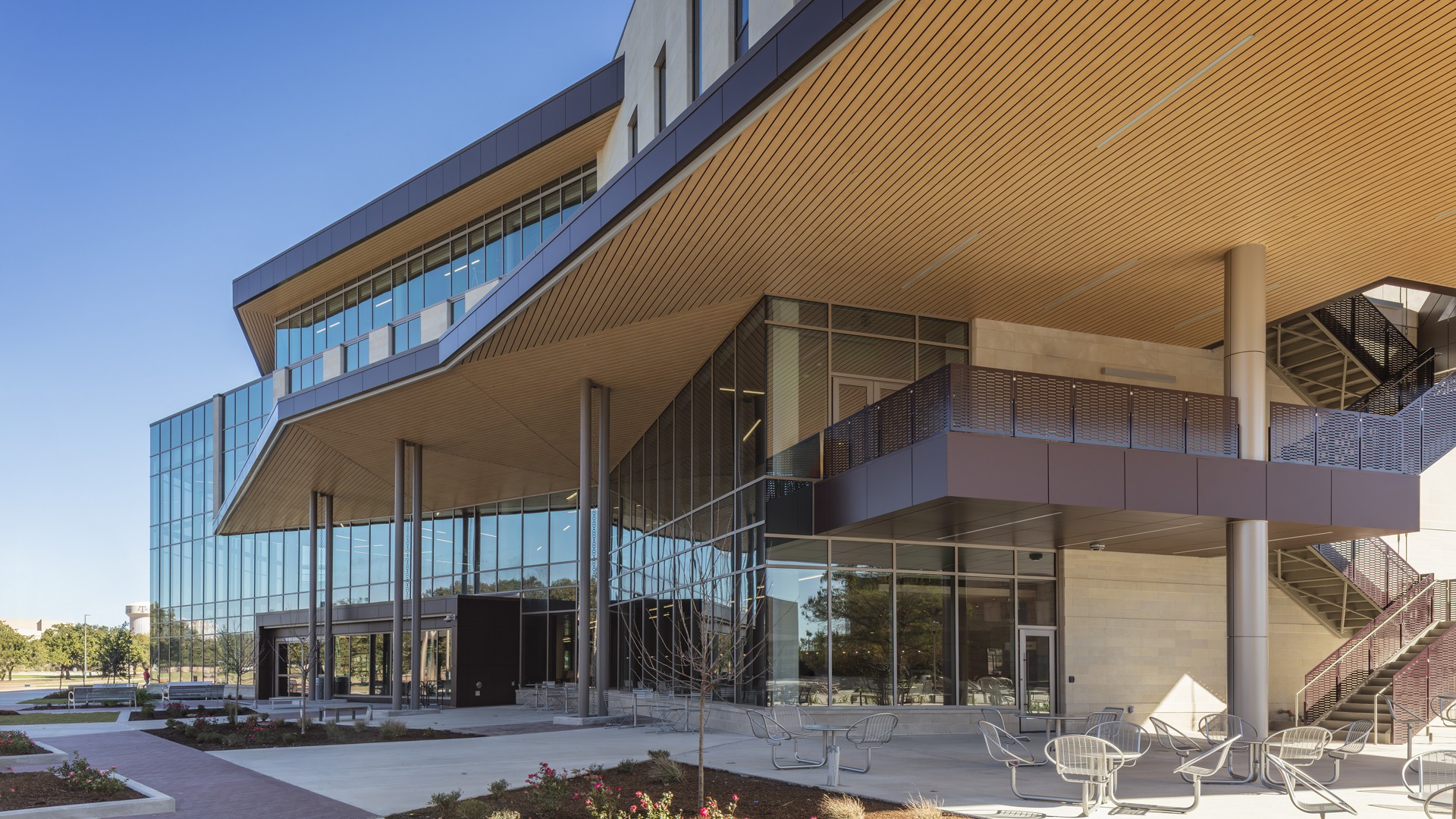 Modern glass and concrete commercial building with outdoor seating and clear sky.