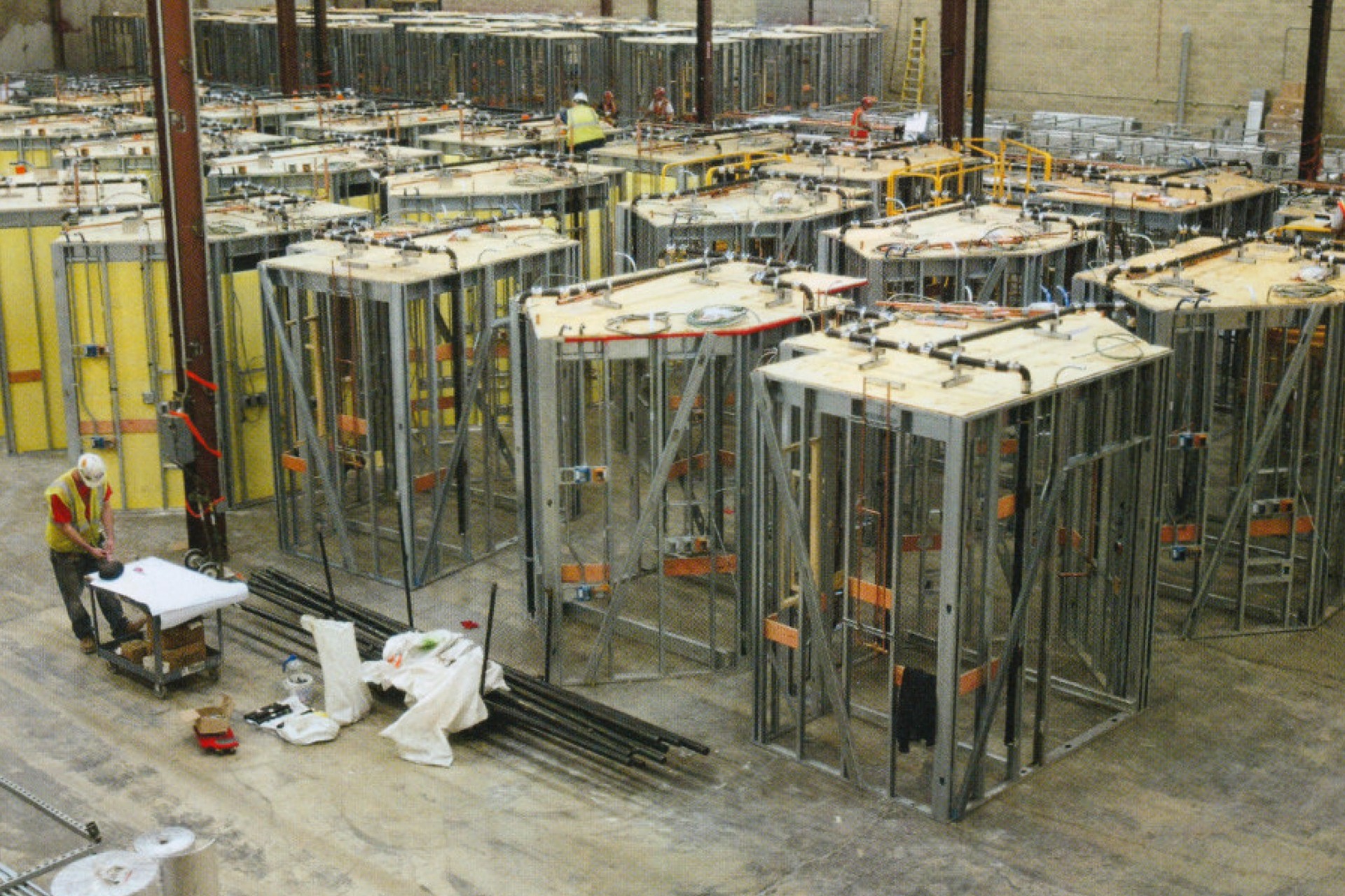 Industrial warehouse with metal frame structures and workers Factory floor with workers assembling metal frames for industrial equipment.
