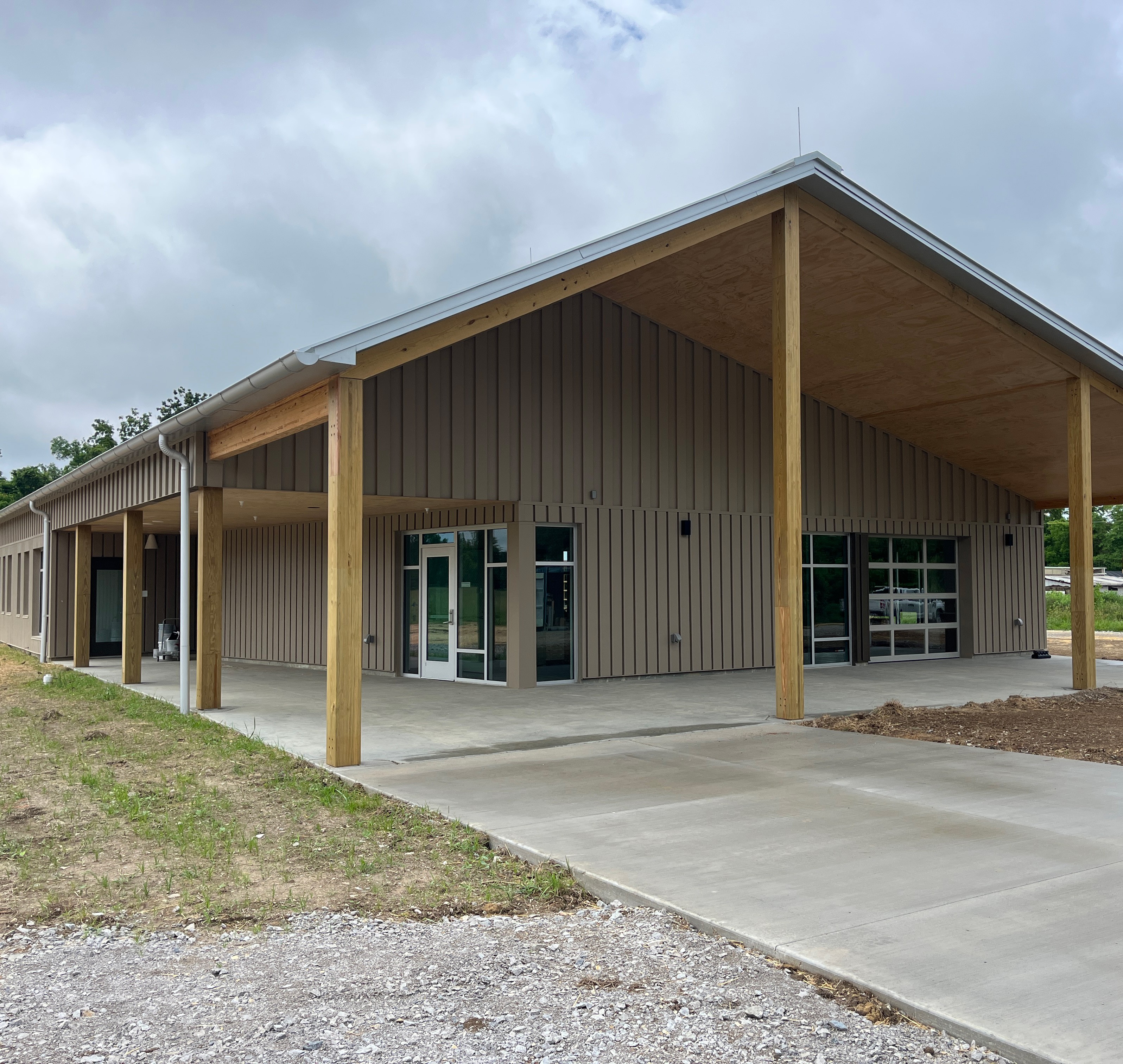 Modern Commercial Building with Covered Entrance and Concrete Path Modern commercial building with wood pillars and large glass doors under a sloped roof.