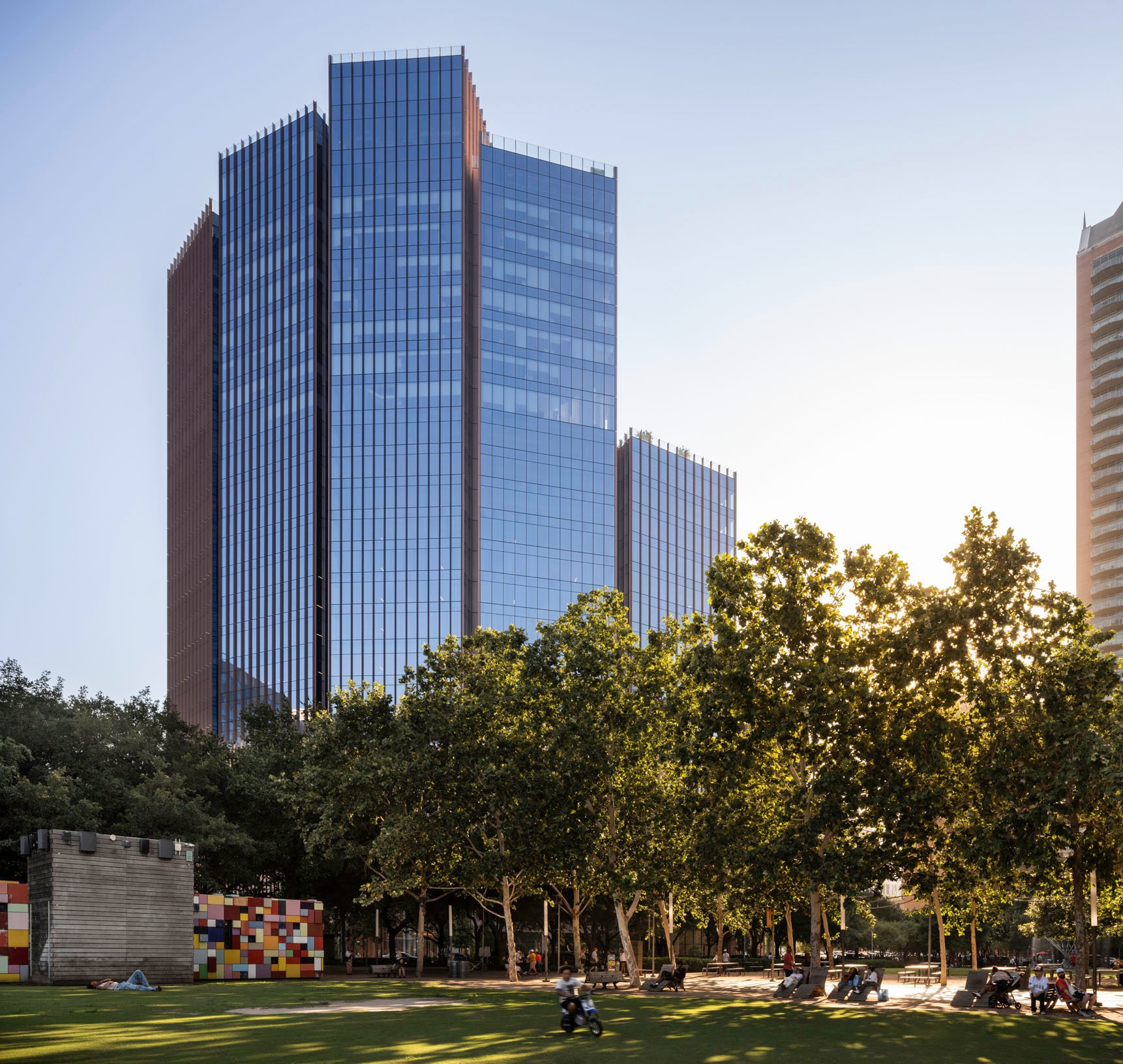 Modern Glass Office Building with Park and Trees at Sunset Modern glass skyscraper behind green trees in a sunny urban park with people relaxing.