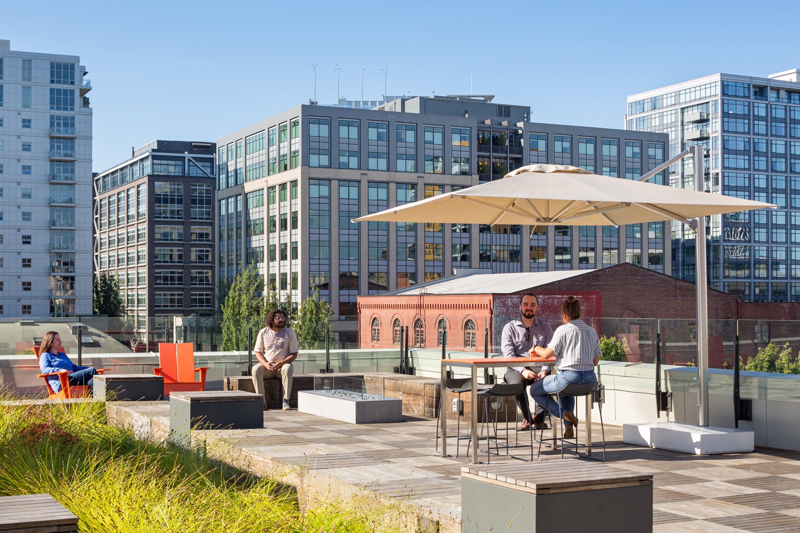 Rooftop Office Space with City Views and Outdoor Seating Rooftop terrace with people socializing, surrounded by modern buildings in a sunny urban setting.