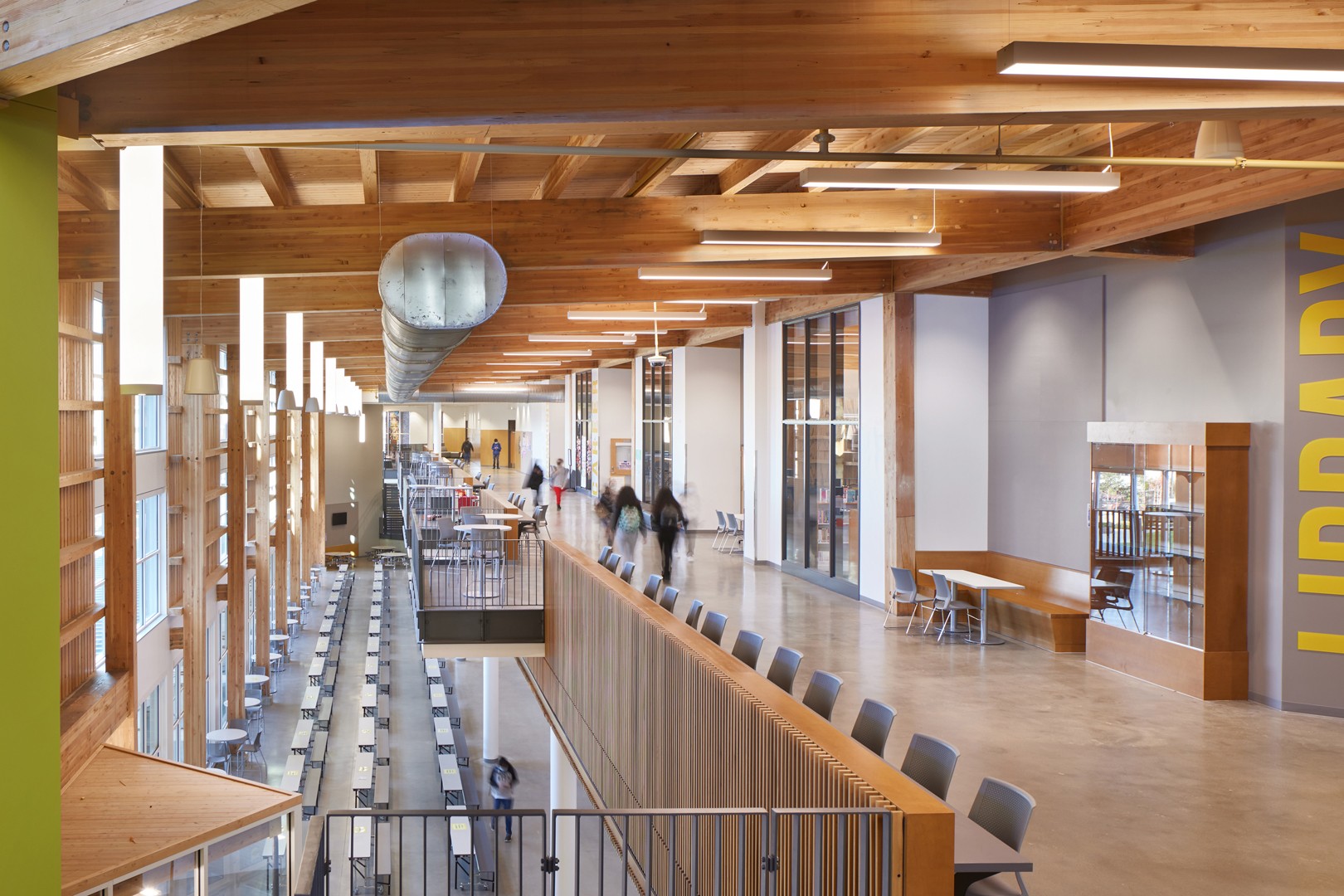 Our Highline High School project in Burien, Washington. Modern library interior with wooden beams, glass windows, seating areas, and a large "Library" sign.