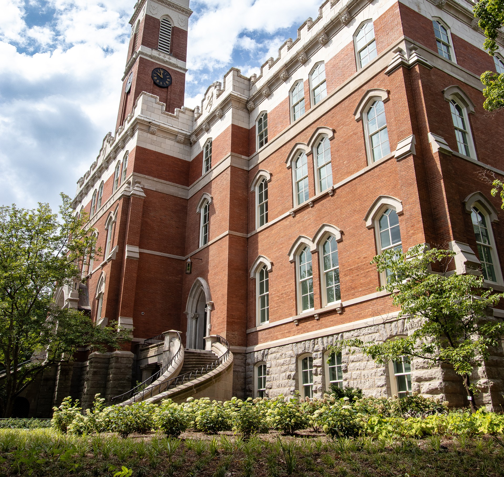 Historic Red Brick University Building with Clock Tower Exterior Historic red brick building with clock tower and curved stone staircase surrounded by greenery.