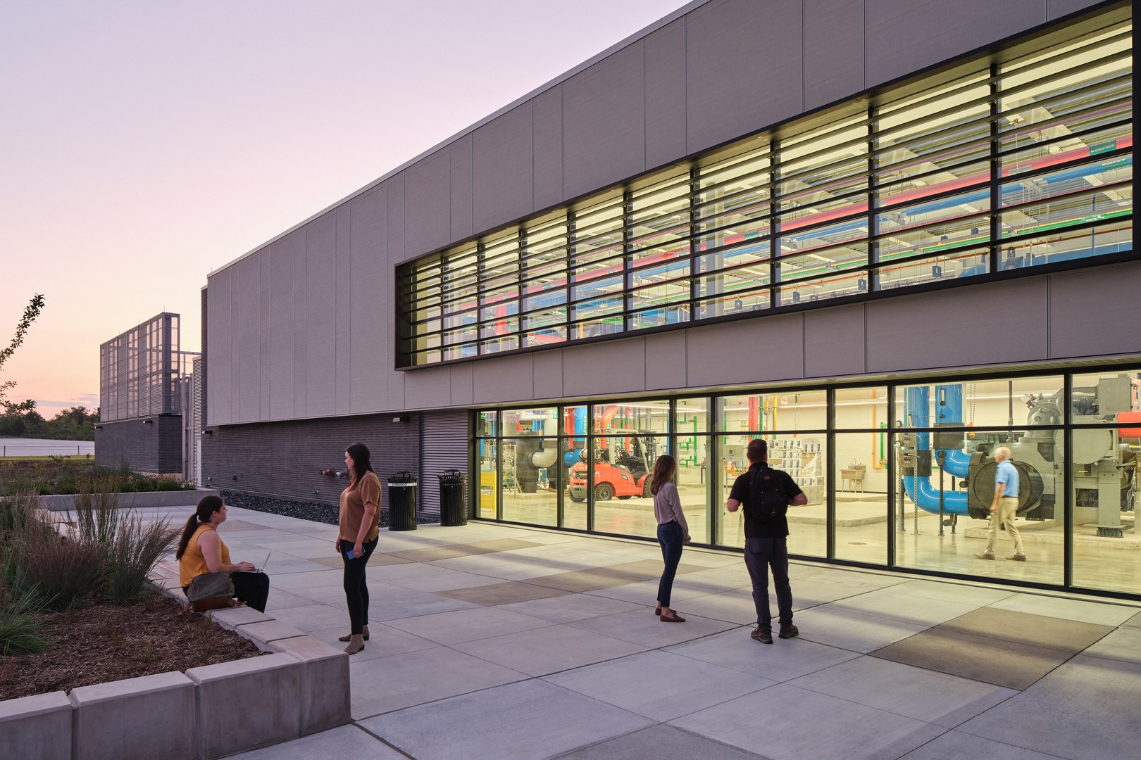 Modern Industrial Building with People Outside at Dusk Modern industrial building exterior with people standing and talking outside at dusk.