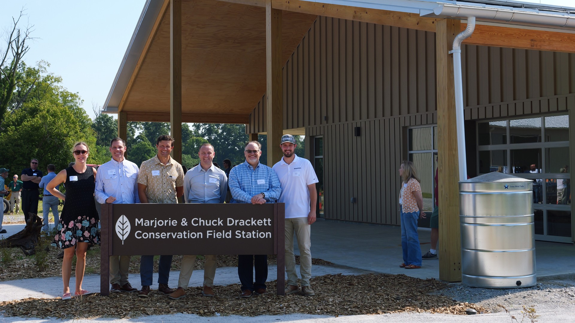 Group of six people standing outdoors holding a sign for Marjorie & Chuck Drackett Conservation Field Station.