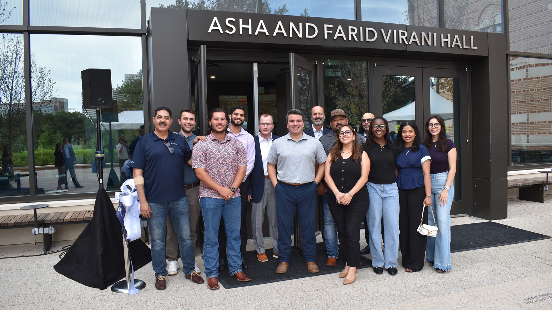 Group of diverse professionals standing outside Asha and Farid Virani Hall, smiling.