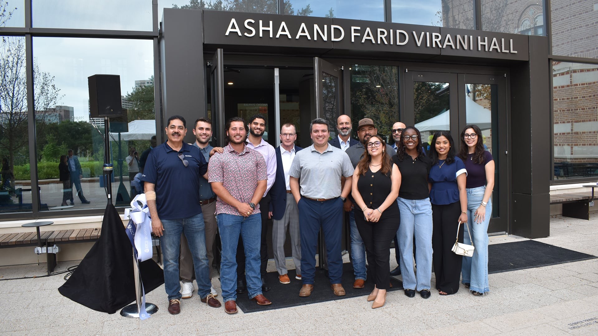 Grand Opening of Asha and Farid Virani Hall Group of diverse professionals standing outside Asha and Farid Virani Hall, smiling.