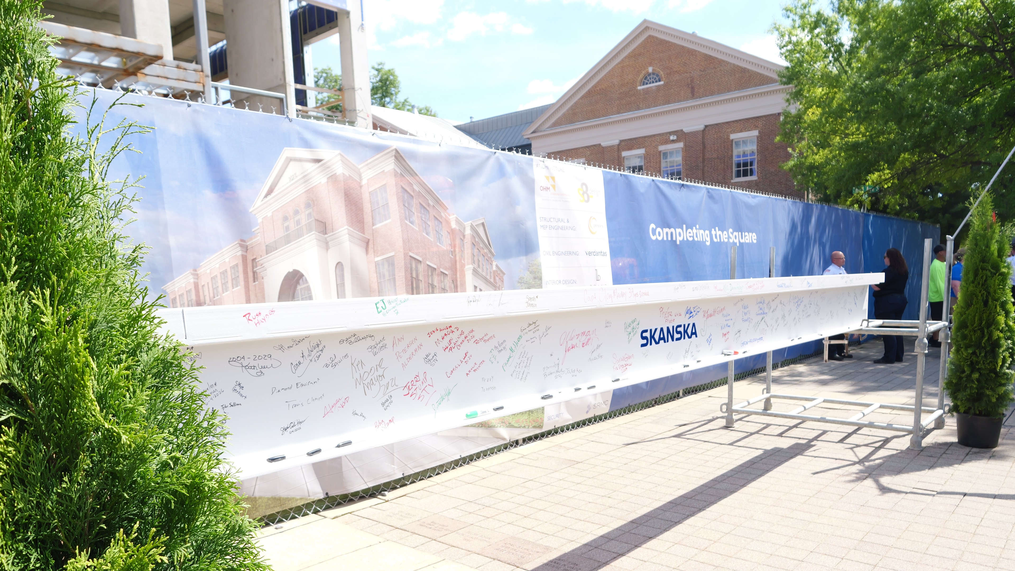 Signed steel beam at a construction site with Skanska logo and building backdrop.
