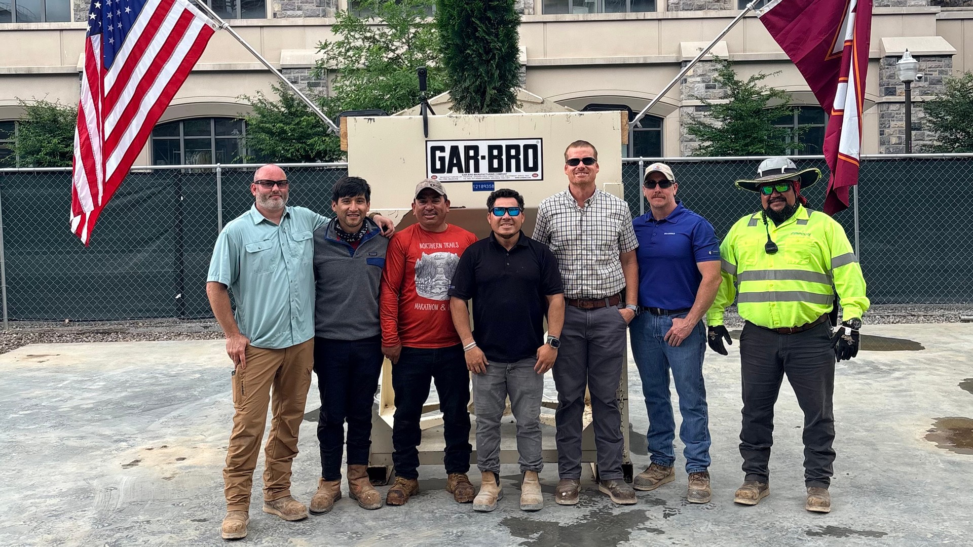 Group of seven construction workers posing outdoors in front of a GAR-BRO machine.