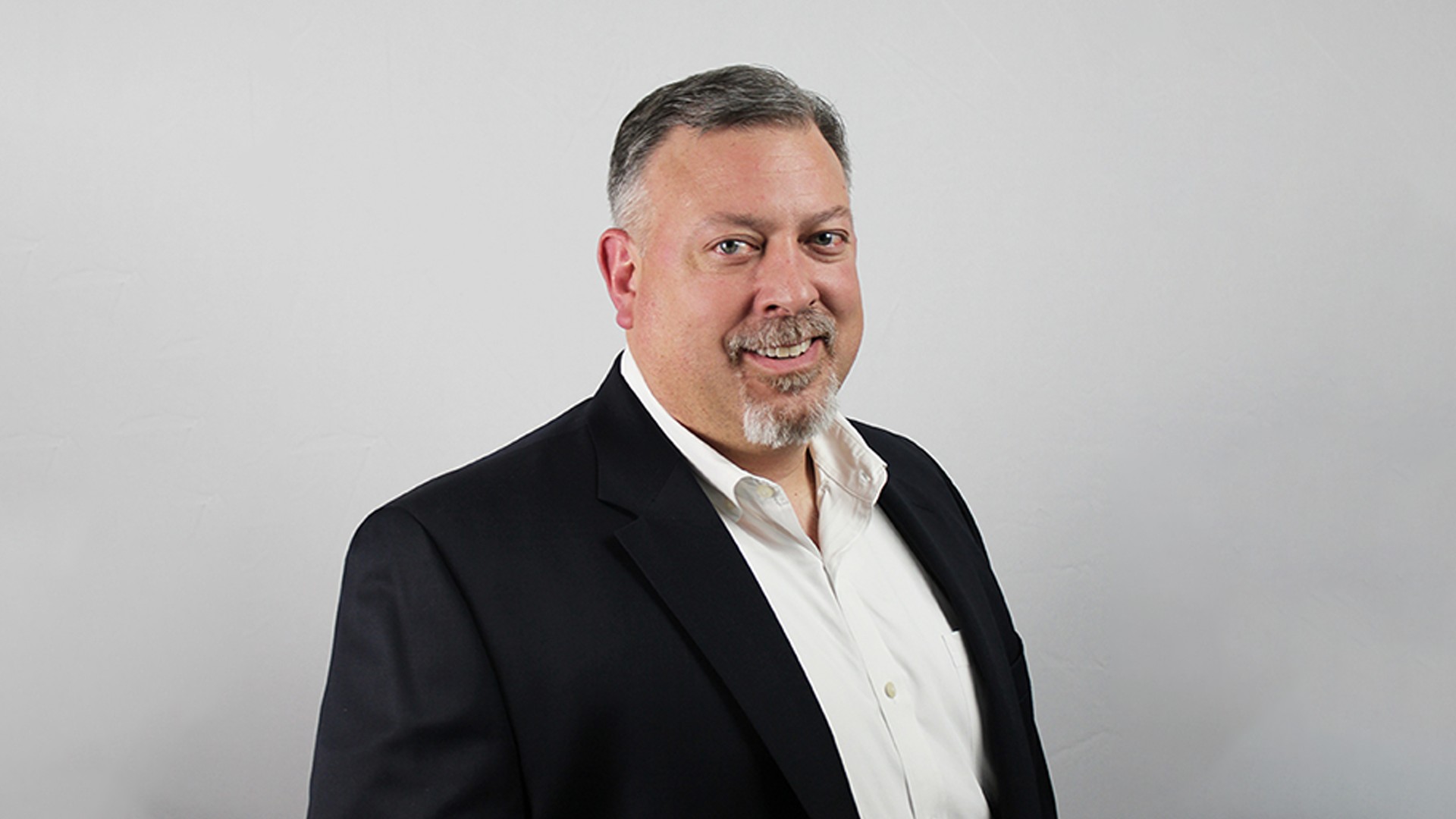 Professional man in black suit and white shirt on gray background Bryan in a black suit jacket and white shirt against a plain gray background.