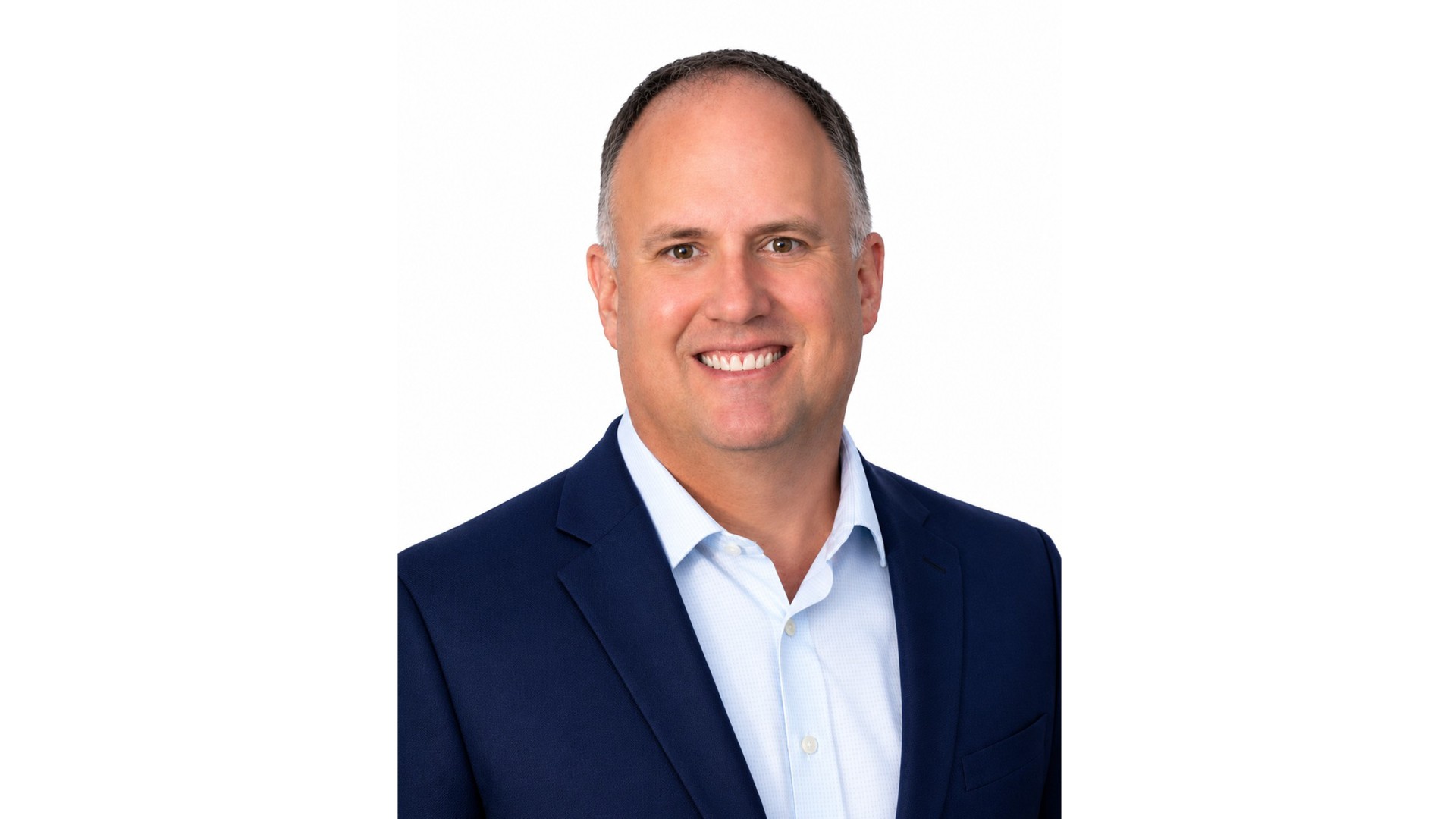 Professional headshot of a smiling man in a navy suit and light blue shirt on white background.
