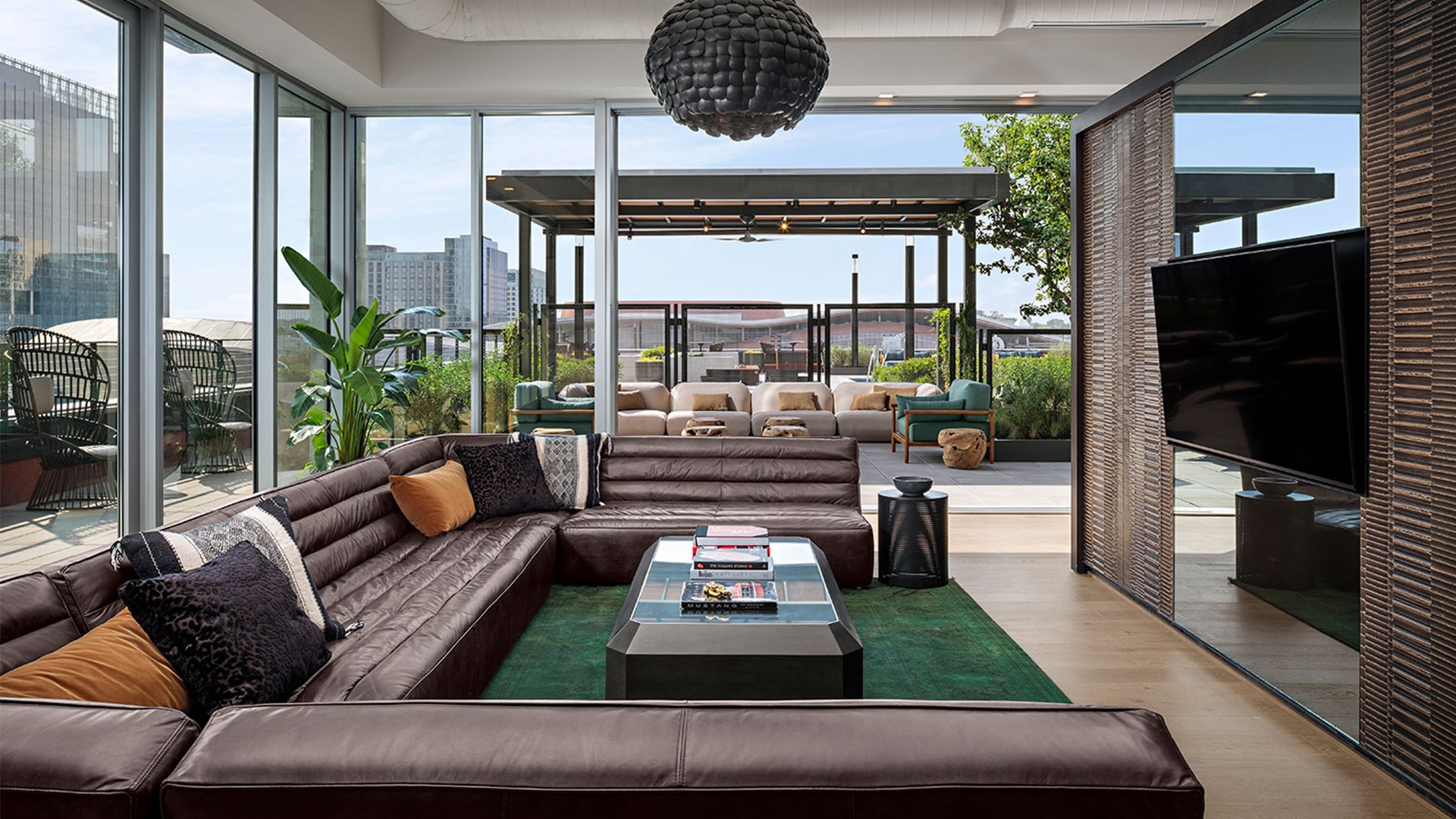 Modern living room with large leather sectional, glass walls, and city view balcony.