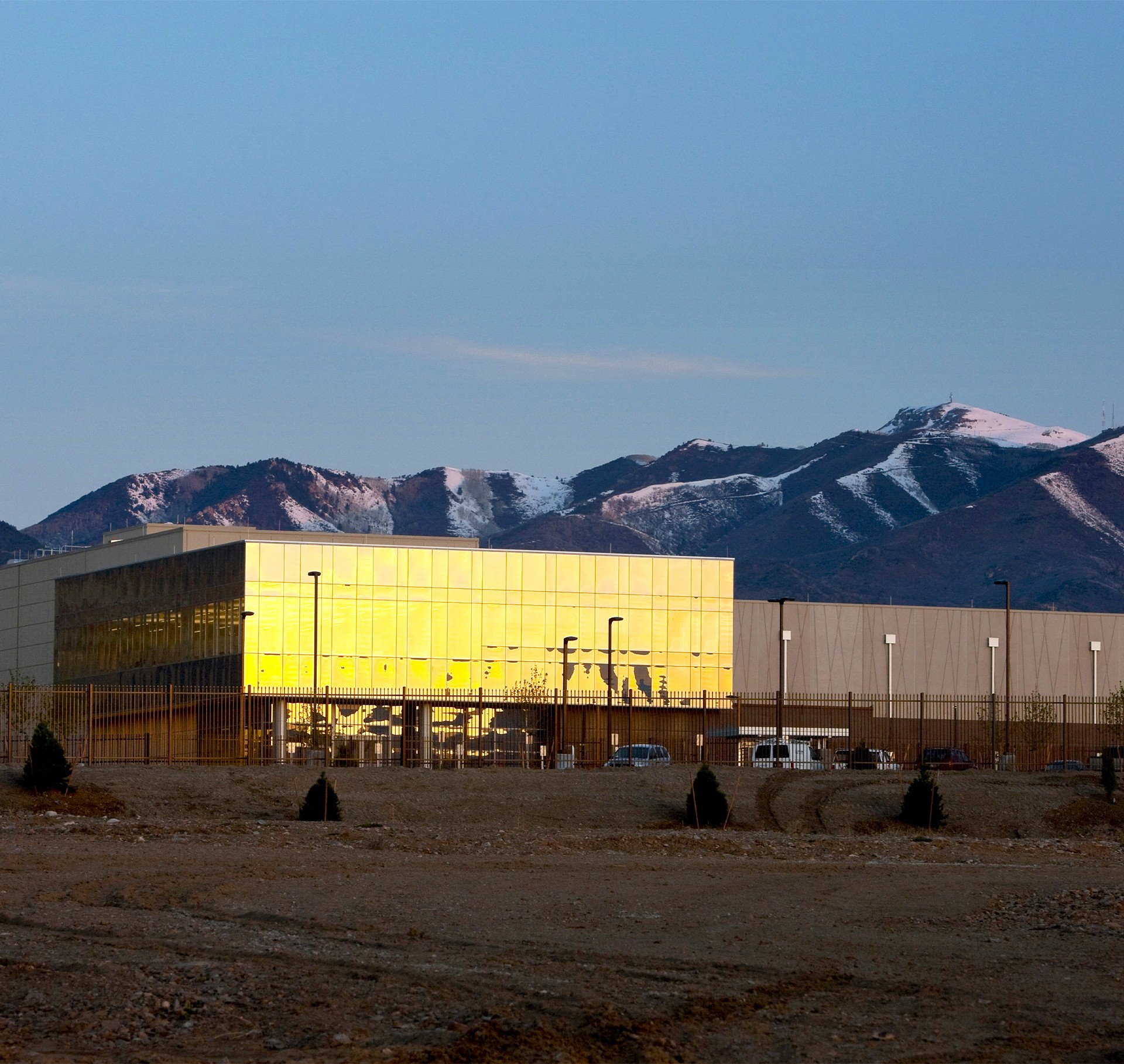 Modern Golden Glass Building with Mountain Backdrop at Sunset Modern industrial building with reflective golden glass panels set against mountain backdrop.
