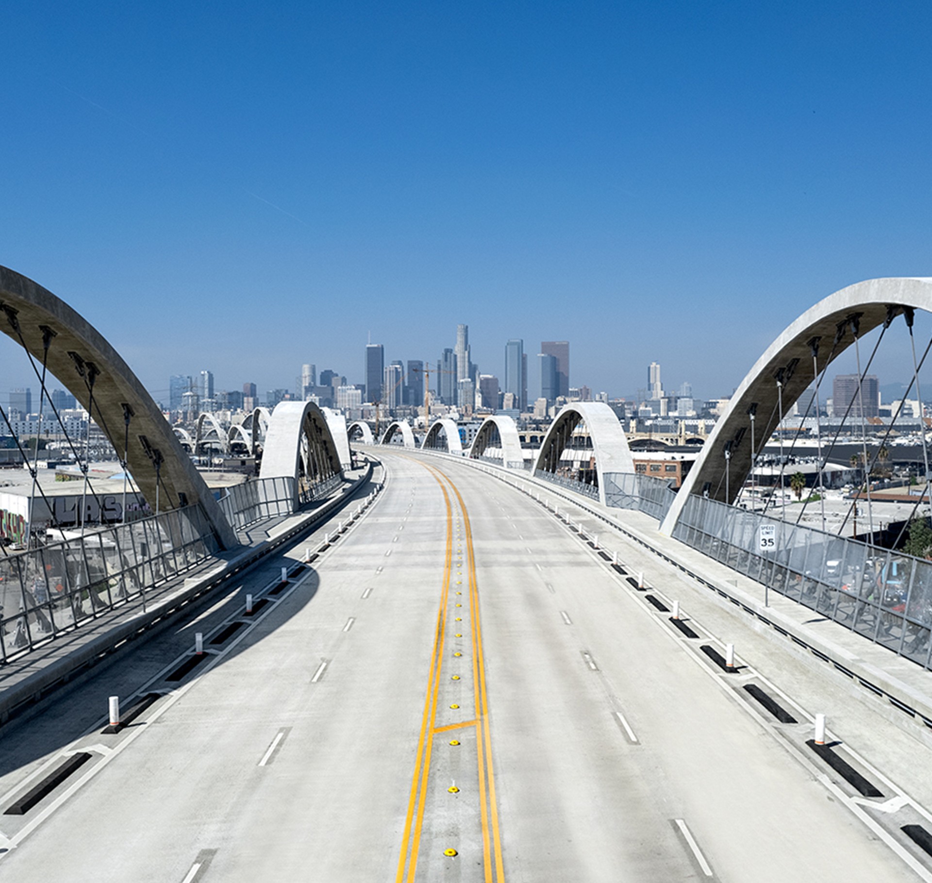 Empty bridge with city skyline under clear blue sky, Los Angeles Sixth Street bridge leading to a city skyline under a clear blue sky.