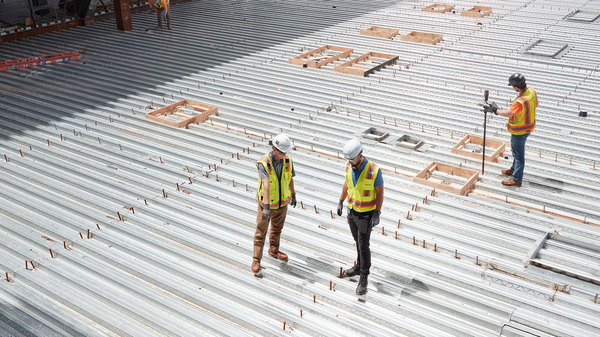 Construction workers wearing safety gear inspecting metal decking at a building site.