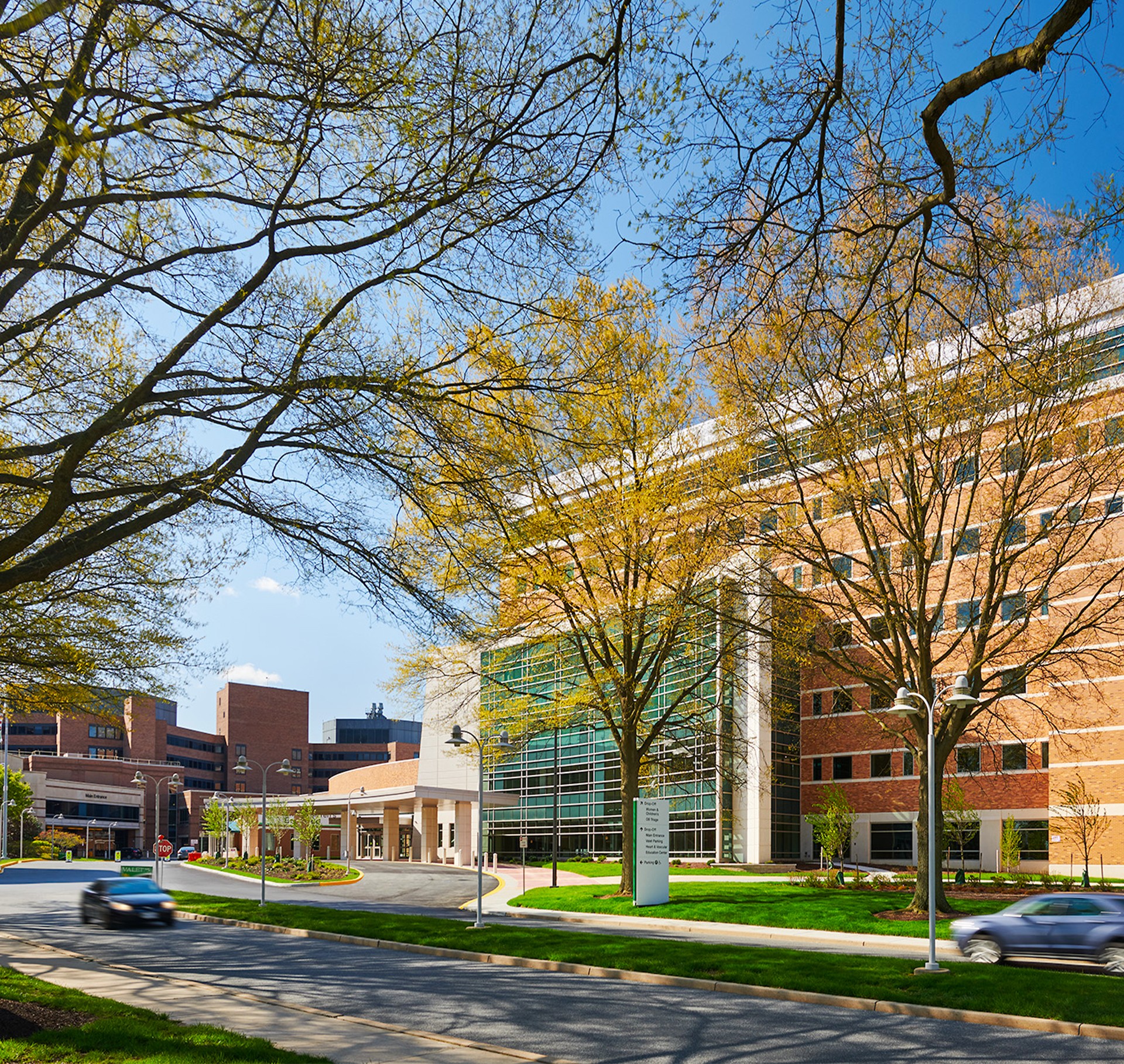 Modern hospital building with trees and cars on a sunny day under a clear blue sky.