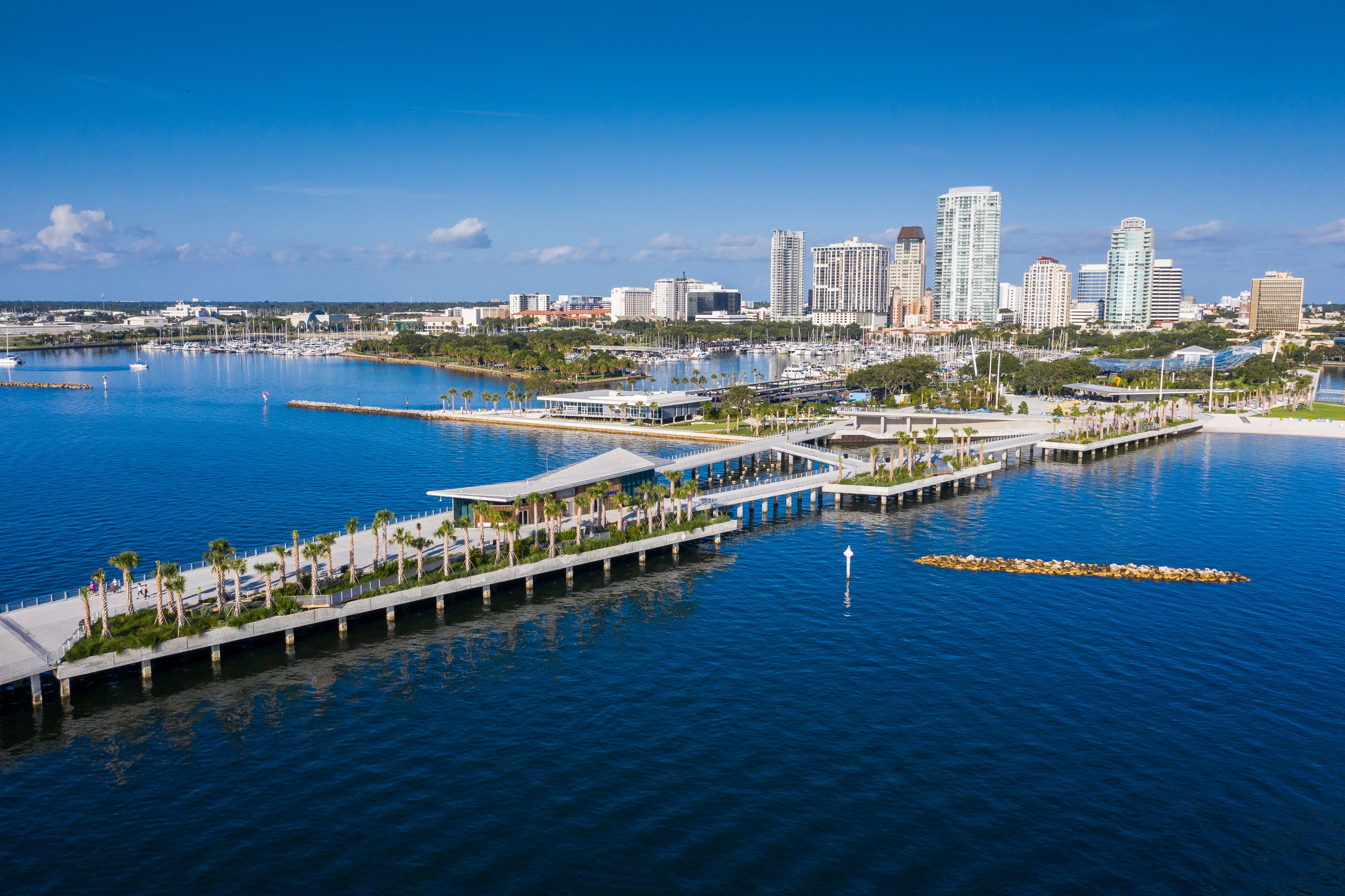 Aerial view of a coastal city with waterfront parks, piers, and modern high-rise buildings.