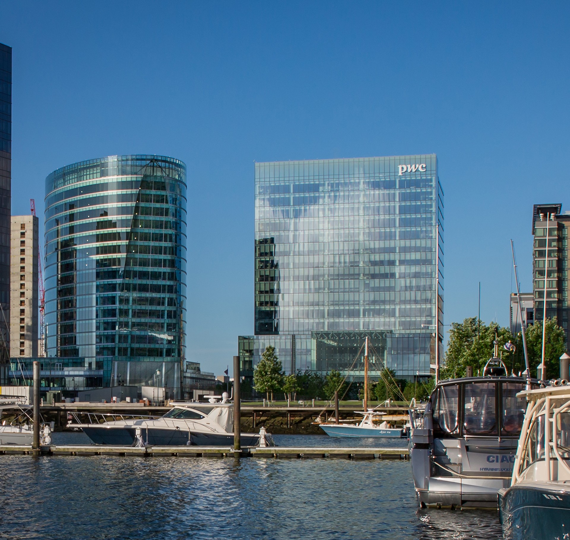 Modern waterfront cityscape with PwC glass building reflection Seaport glass office buildings and boats docked at a marina under a clear blue sky.