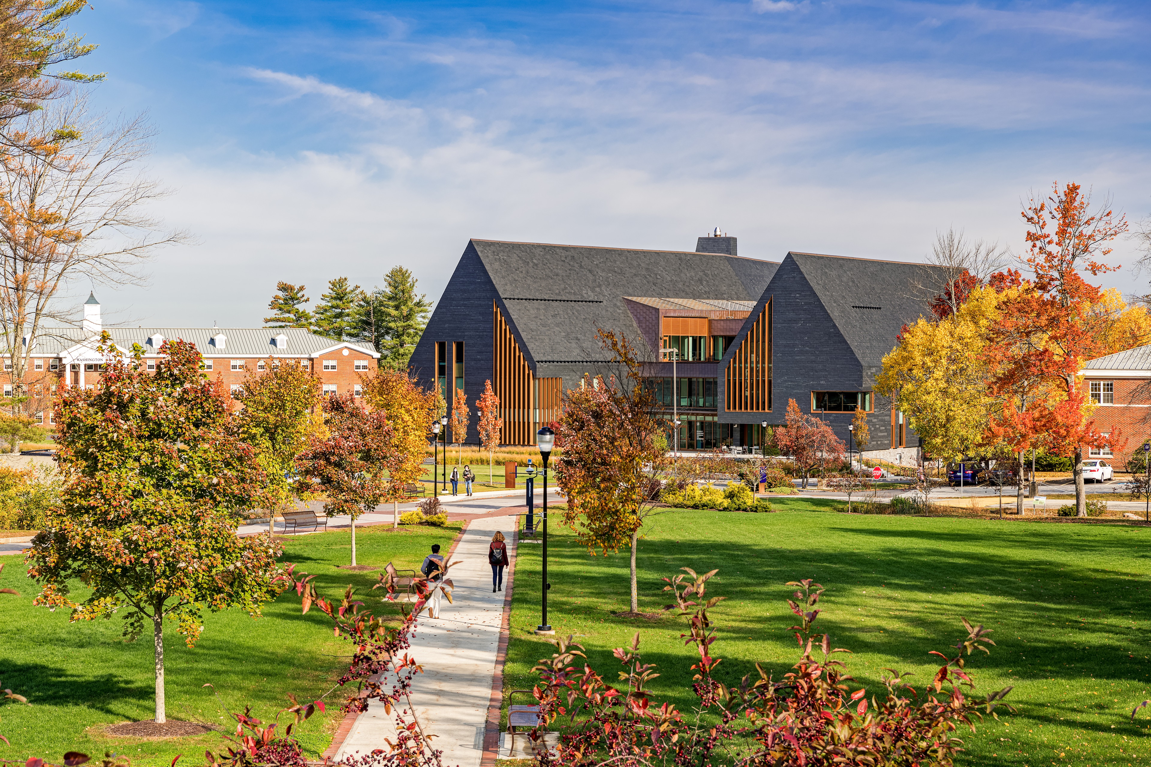 Modern campus building with people walking on pathways surrounded by autumn trees.