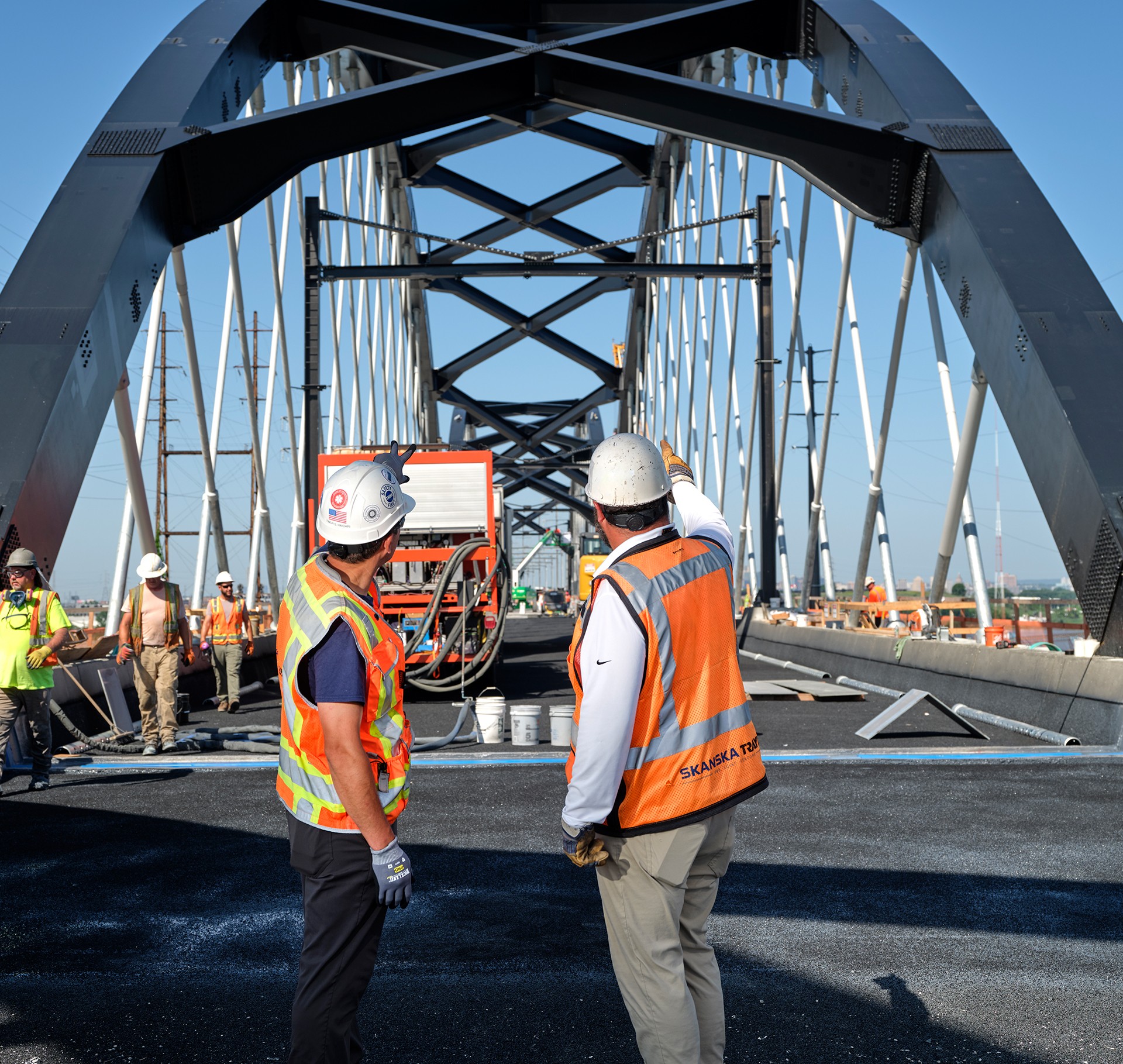 Construction workers inspecting progress on steel bridge project Construction workers wearing safety gear inspecting a steel bridge under clear sky.