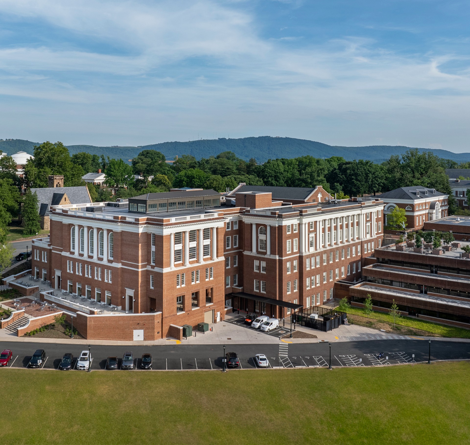 Large historic brick building with white accents, surrounded by greenery and parked cars.