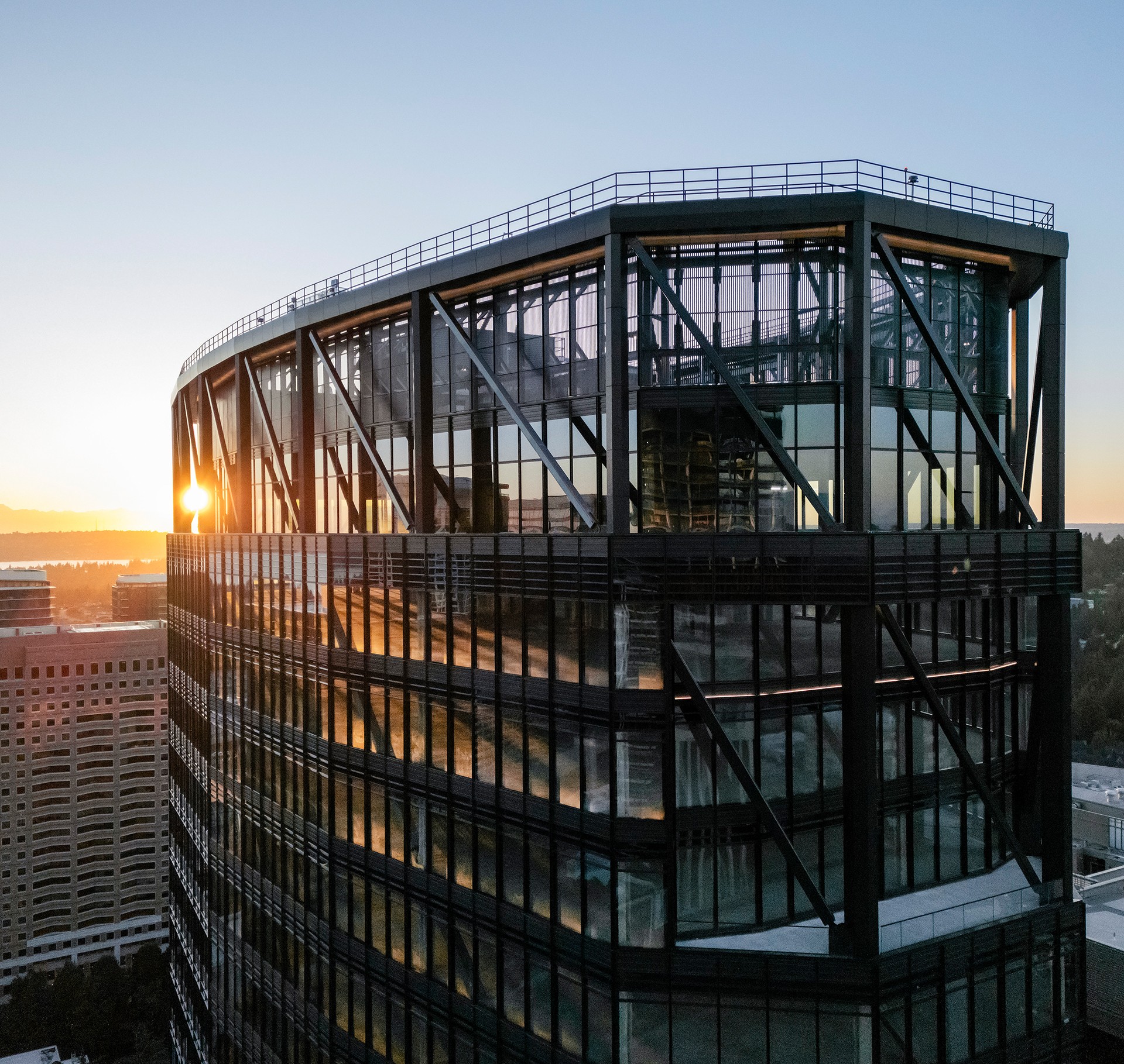 Office Building at Sunset with Reflective Glass Facade A glass skyscraper with steel framework reflecting sunset in an urban setting.
