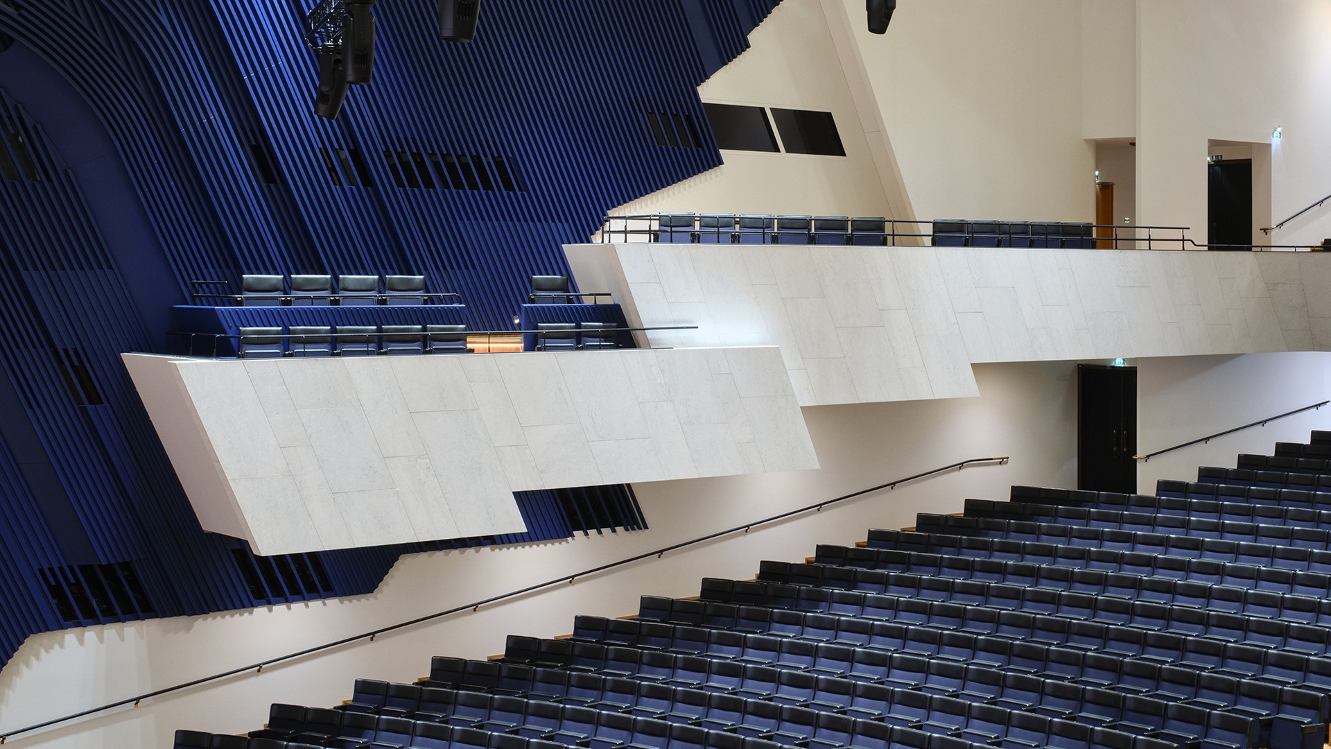Moderni auditoriotila sinisillä ja valkoisilla istuintasoilla sekä geometrisella arkkitehtonisella suunnittelulla.