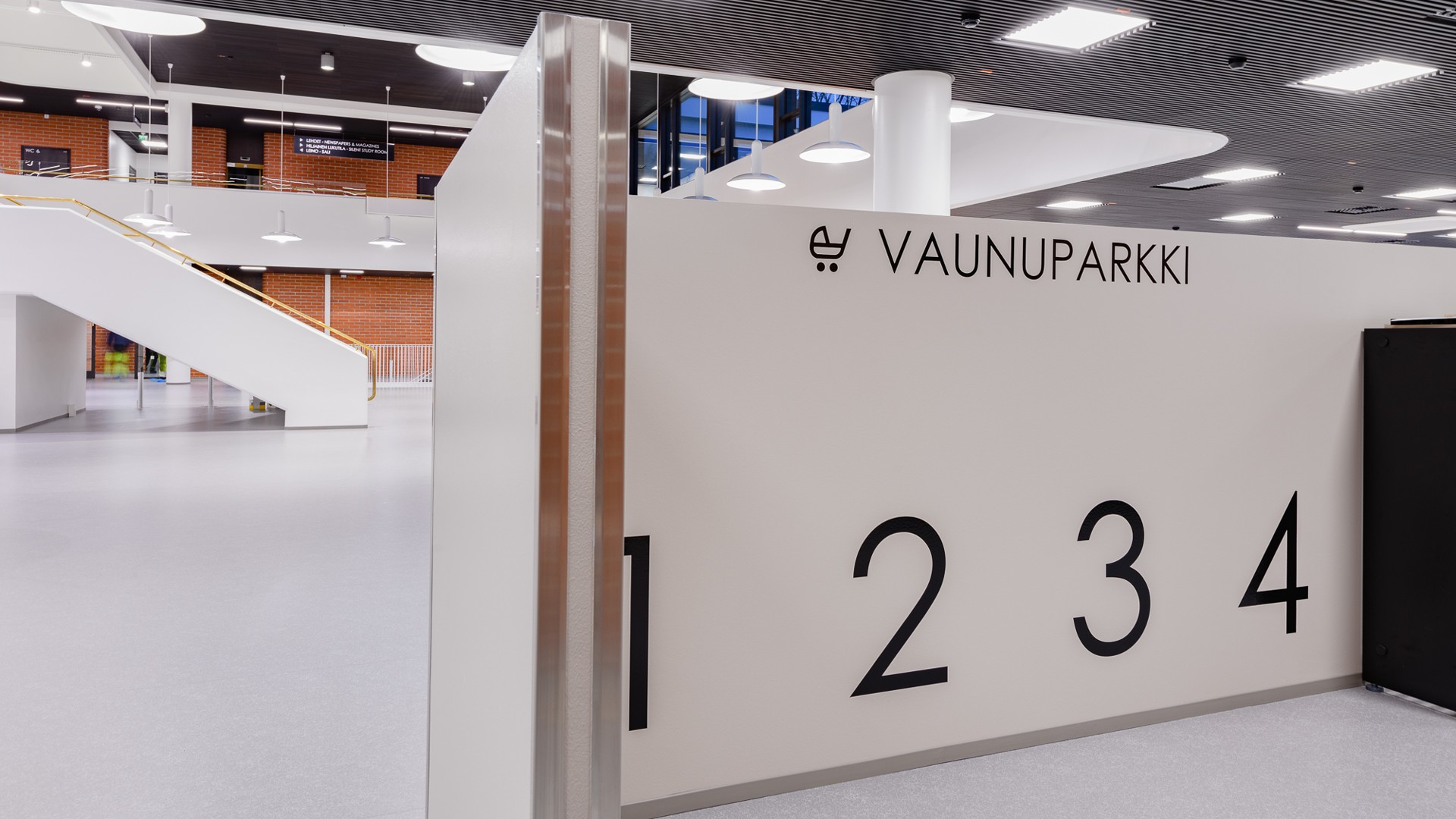 Moderni sisätila, jossa numeroidut osiot pysäköintiä varten, merkitty "Vaunuparkki" valkoiselle seinälle.