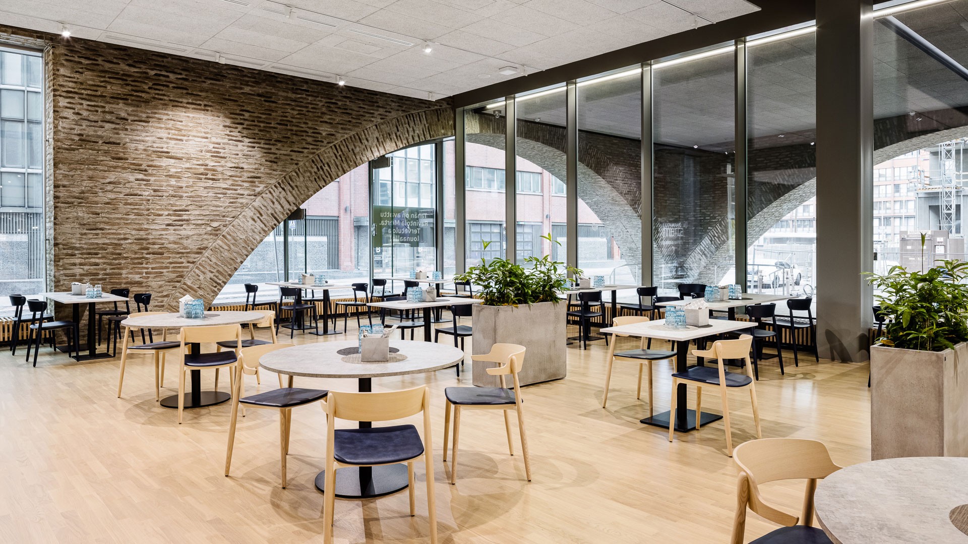 Moderni ravintola, jossa on puiset lattiat, kaarevat tiiliseinät ja suuret ikkunat; tyylikkäät istuimet.
