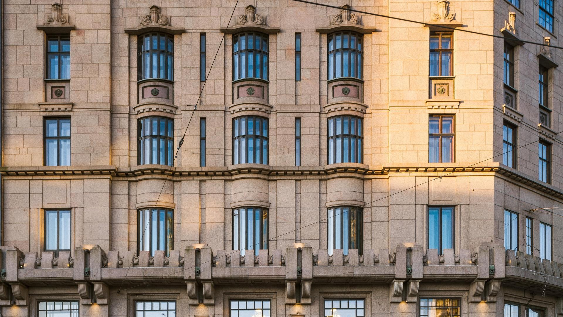 Historiallisen rakennuksen julkisivu, jossa on symmetriset ikkunat ja koristeelliset arkkitehtoniset yksityiskohdat auringonvalossa.