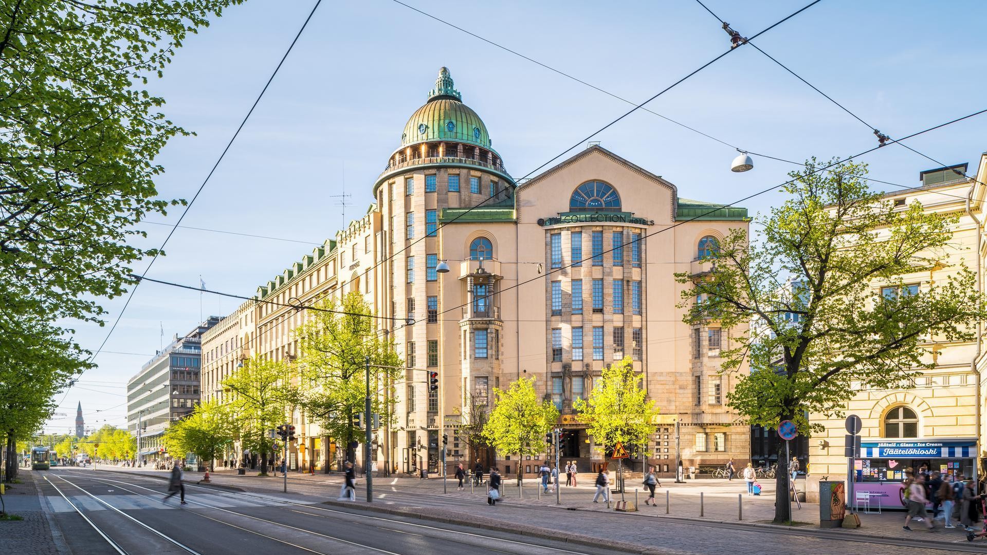 Kuva Helsingin keskustan tiestä, jossa on raitiovaunukiskot, jalankulkijoita ja näkyvä kupolirakennus kirkkaan taivaan alla.