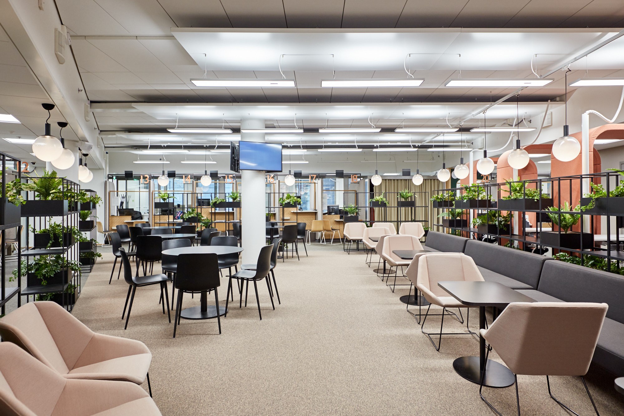 Nykyaikainen coworking-tila, jossa on kasveja, pyöreitä pöytiä ja mukavat istuimet, ihanteellinen yhteistyöhön.