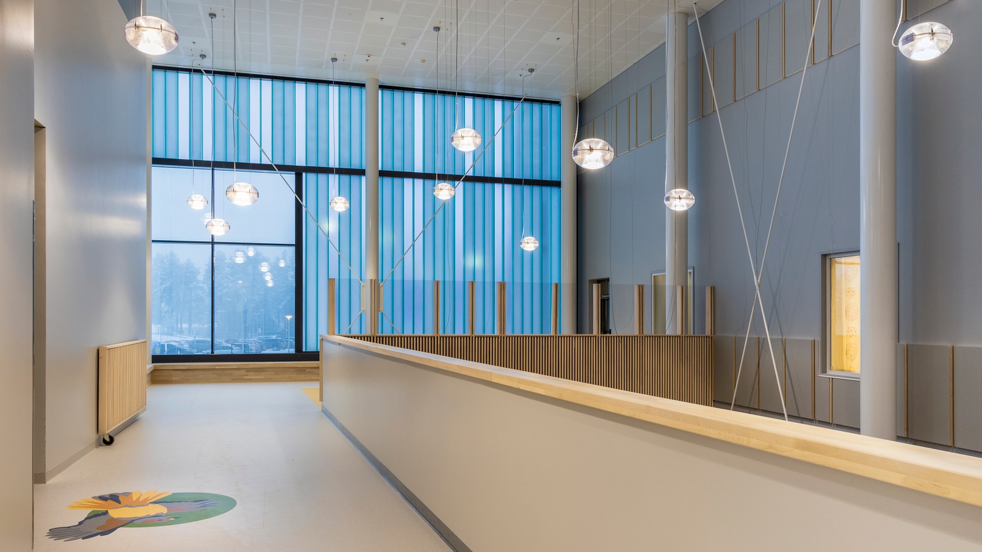 Moderni sisäkäytävä, jossa on suuret siniset ikkunat ja roikkuvat pallomaiset valaisimet.