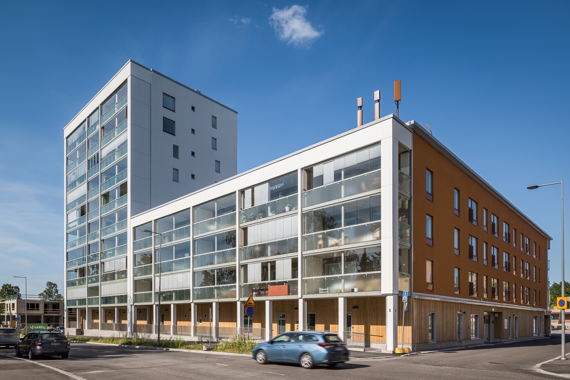 Moderni monikerroksinen asuinkerrostalo suurilla lasi-ikkunoilla kirkkaan sinisen taivaan alla.