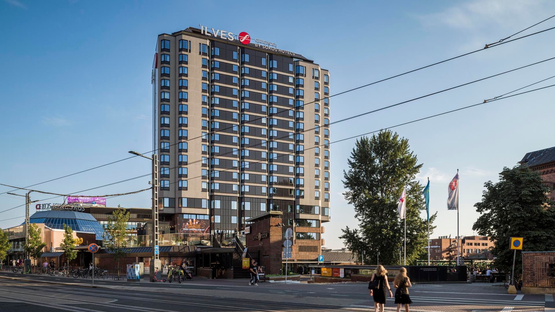 Korkea hotellirakennus, jossa on moderni arkkitehtuuri, varustettuna "Ilves"-kyltillä, kirkkaan sinisen taivaan alla.