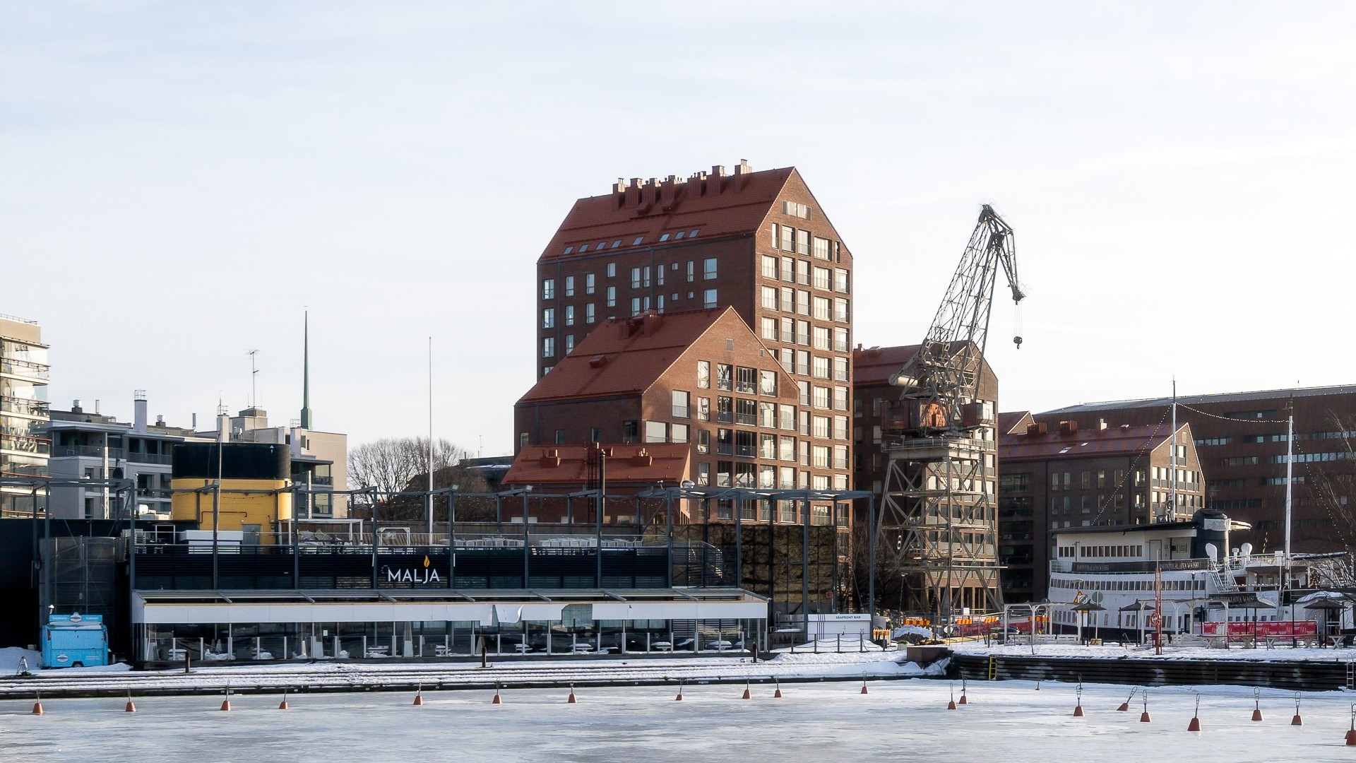 Modernit rantarakennukset, joissa on nosturi, jääpeitteinen vesi ja näkyvissä "Maja"-kyltti.