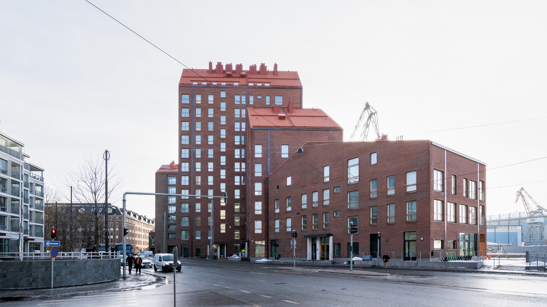 Moderni punatiilinen kerrostalo kaupunkialueella, taustalla teollisuusnosturi.