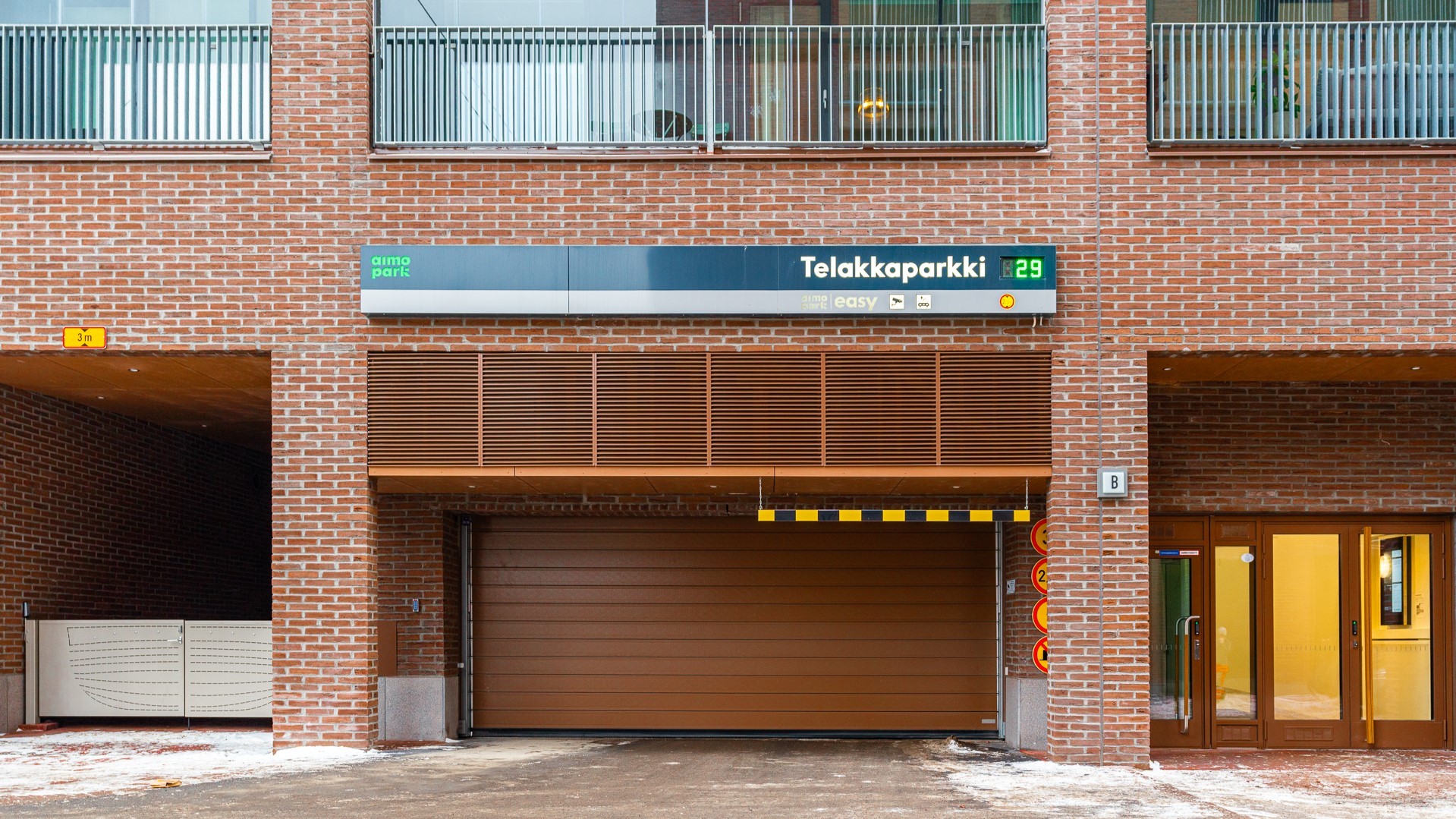 Tiilirakennuksen sisäänkäynti, jossa on autotallin ovi, jossa lukee "Telakkaparkki" ja pysäköintipaikan saatavuusnäyttö.