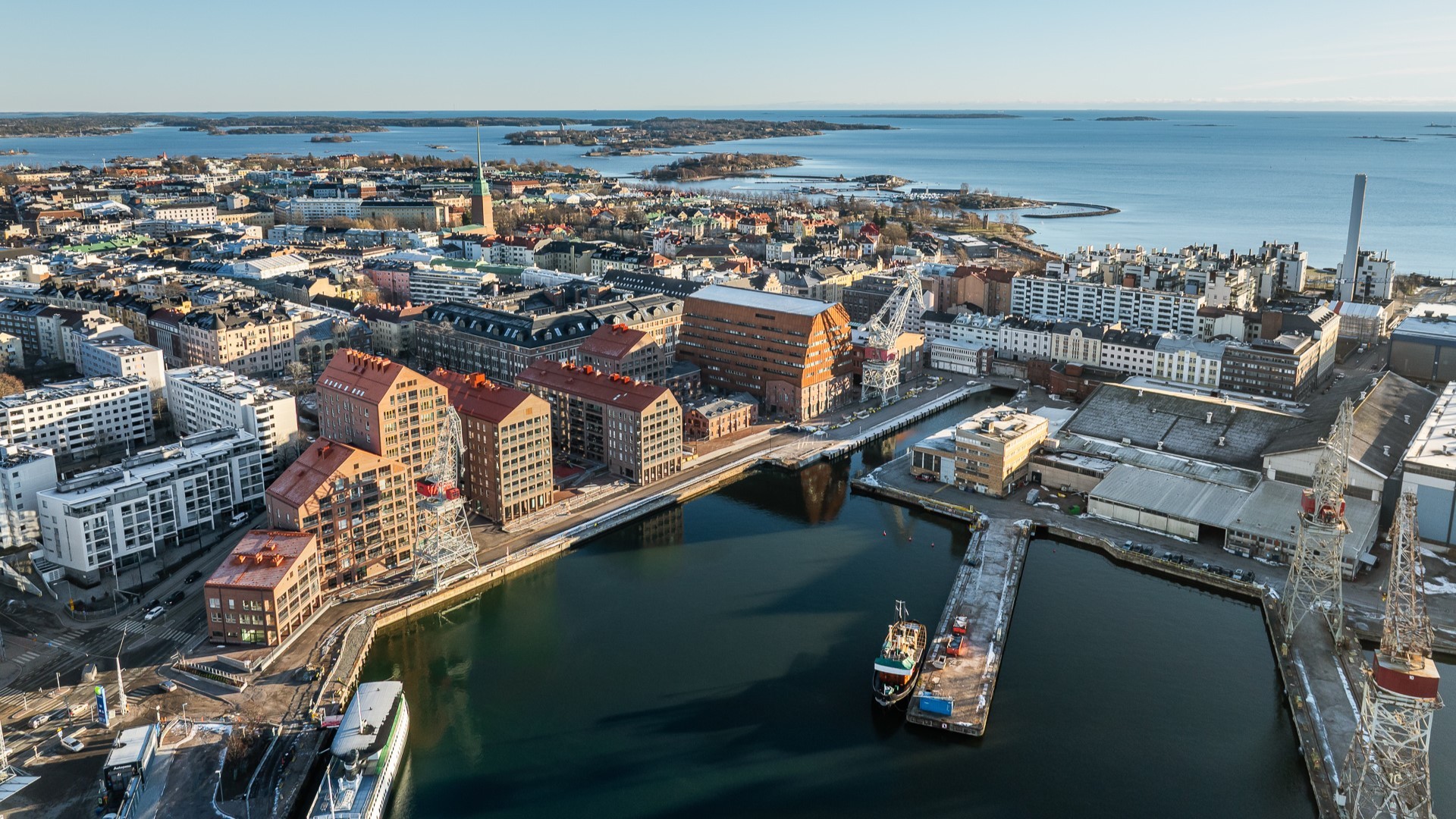 Ilmakuva Helsingin rannasta, jossa on modernia arkkitehtuuria ja maalauksellinen merimaisema taustalla.