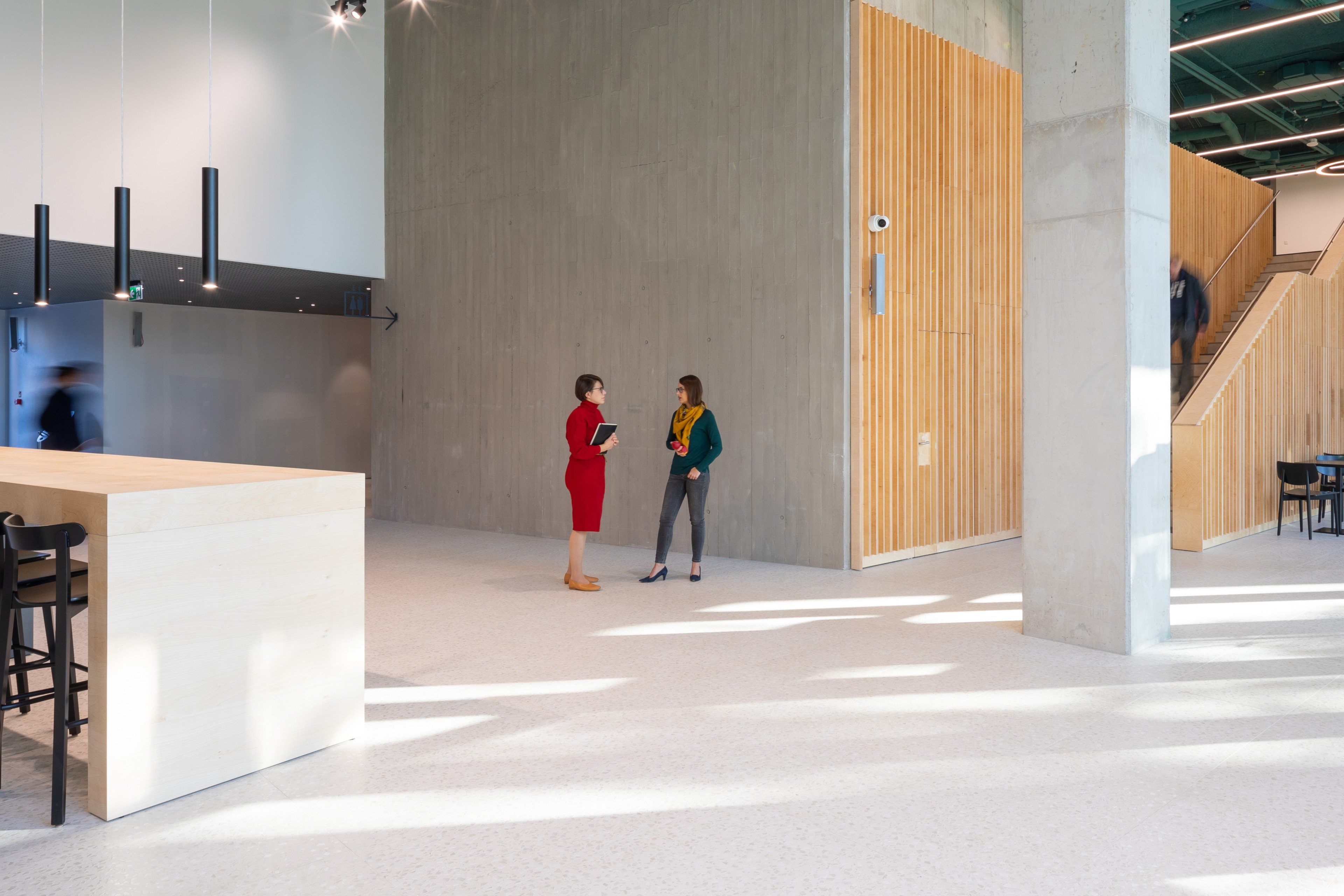 Modern lobby with two people conversing; wooden accents and industrial design elements.