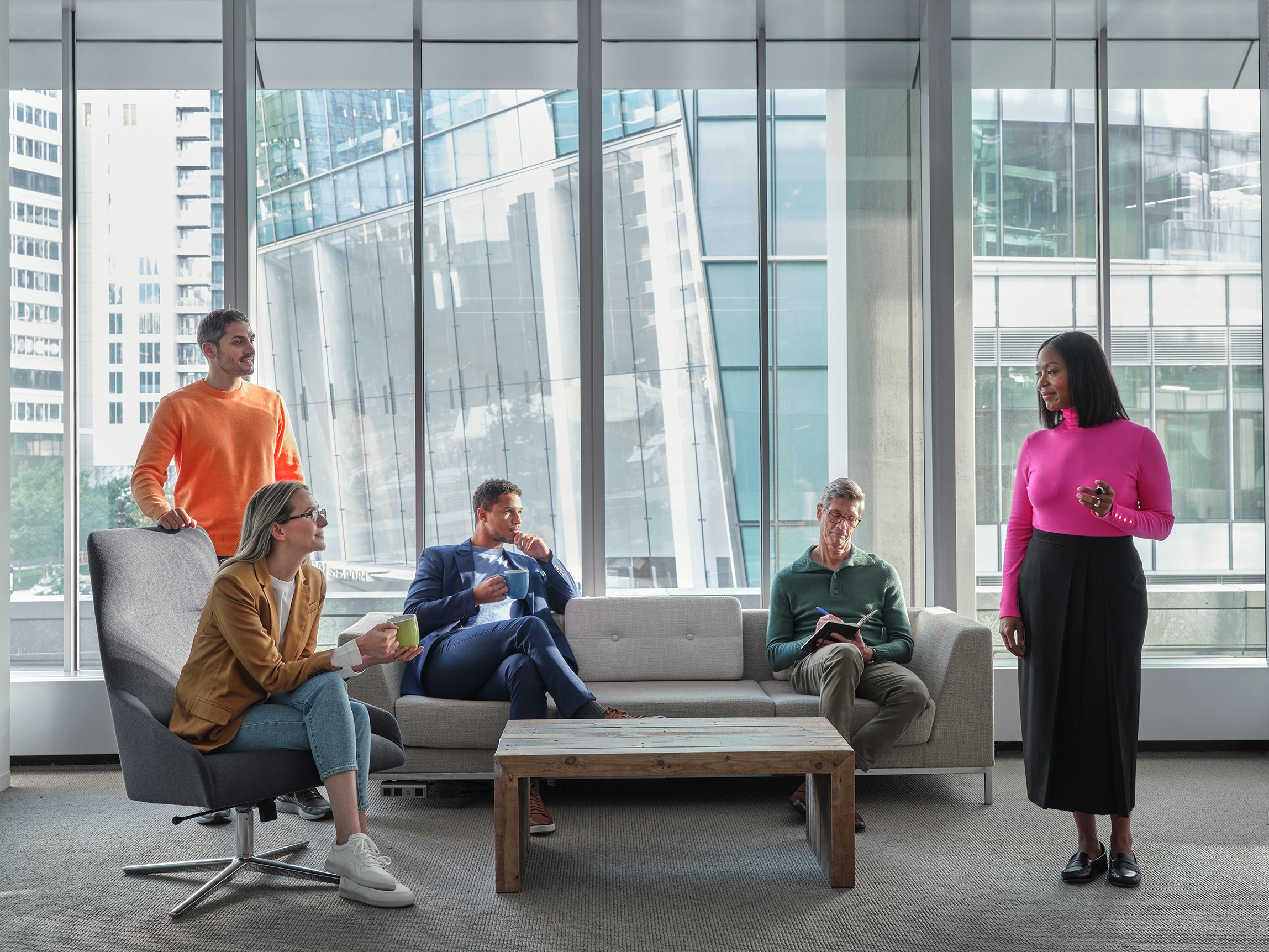 Business meeting in a modern office with five colleagues discussing by large windows.