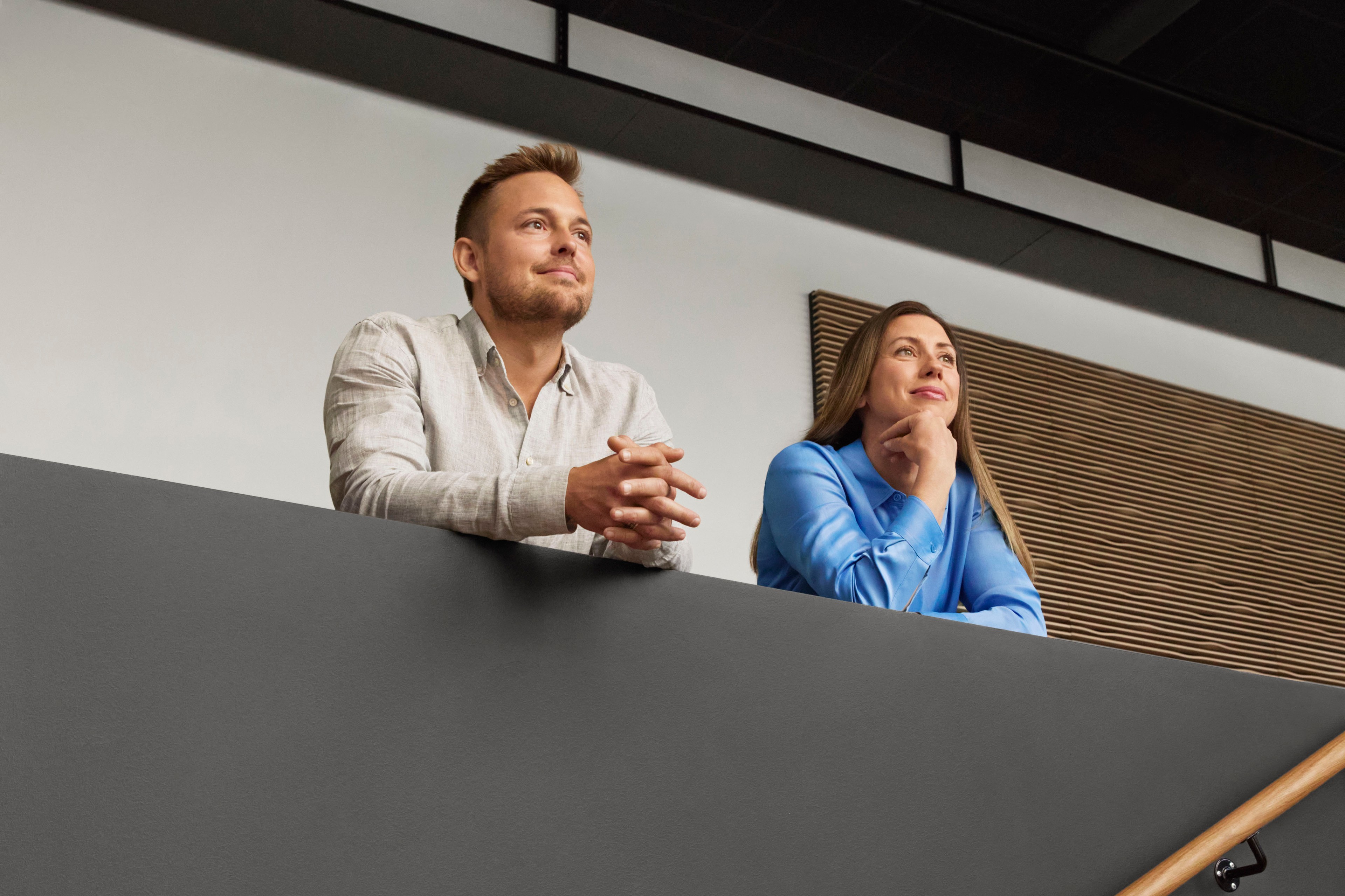 Business Professionals in Modern Office Setting Two individuals stand on a balcony, one wearing a light shirt and the other in a blue outfit.
