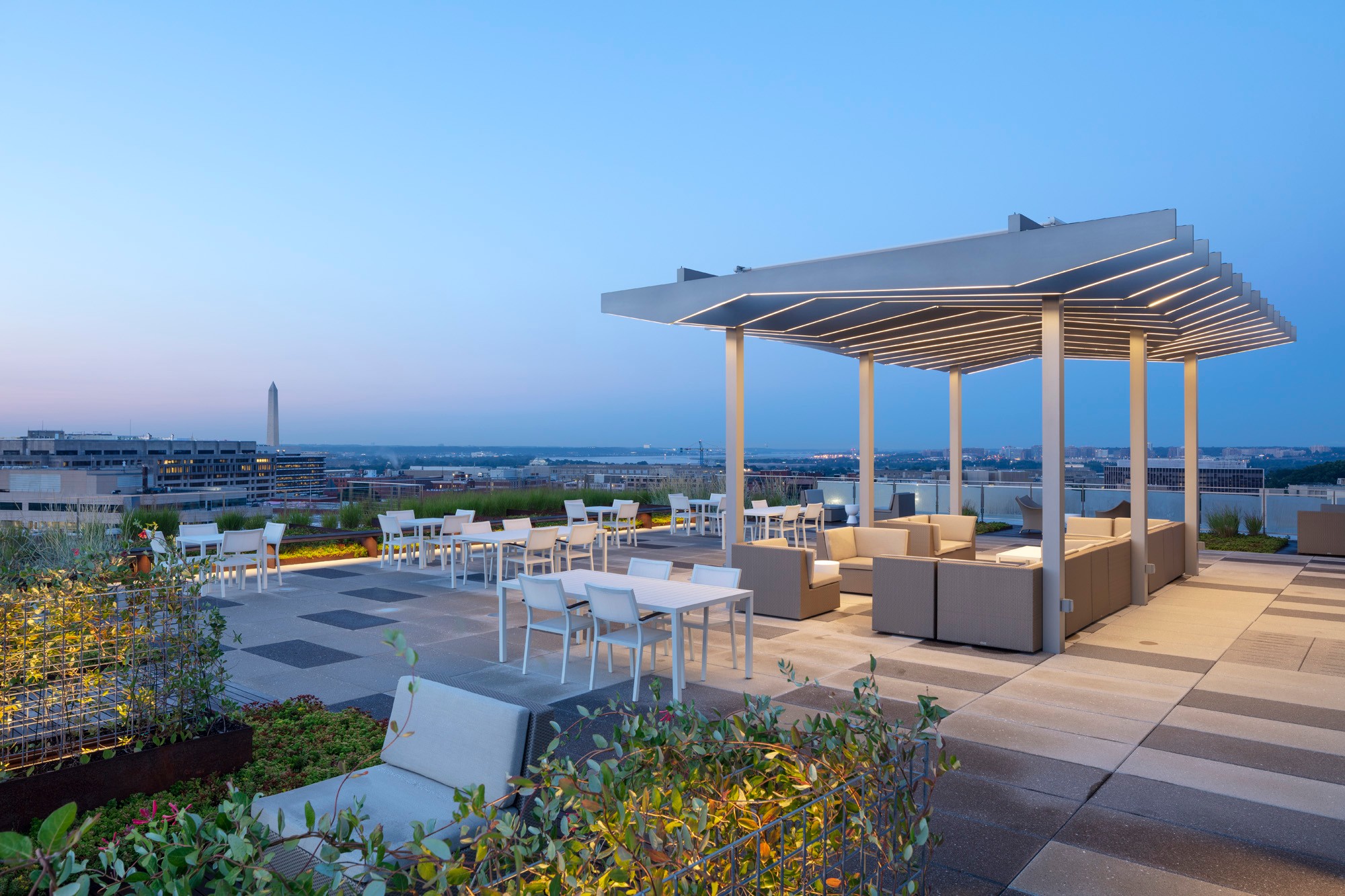 Modern Rooftop Lounge with Stunning City View at Dusk Modern rooftop lounge with seating under a pergola, overlooking a cityscape at dusk.