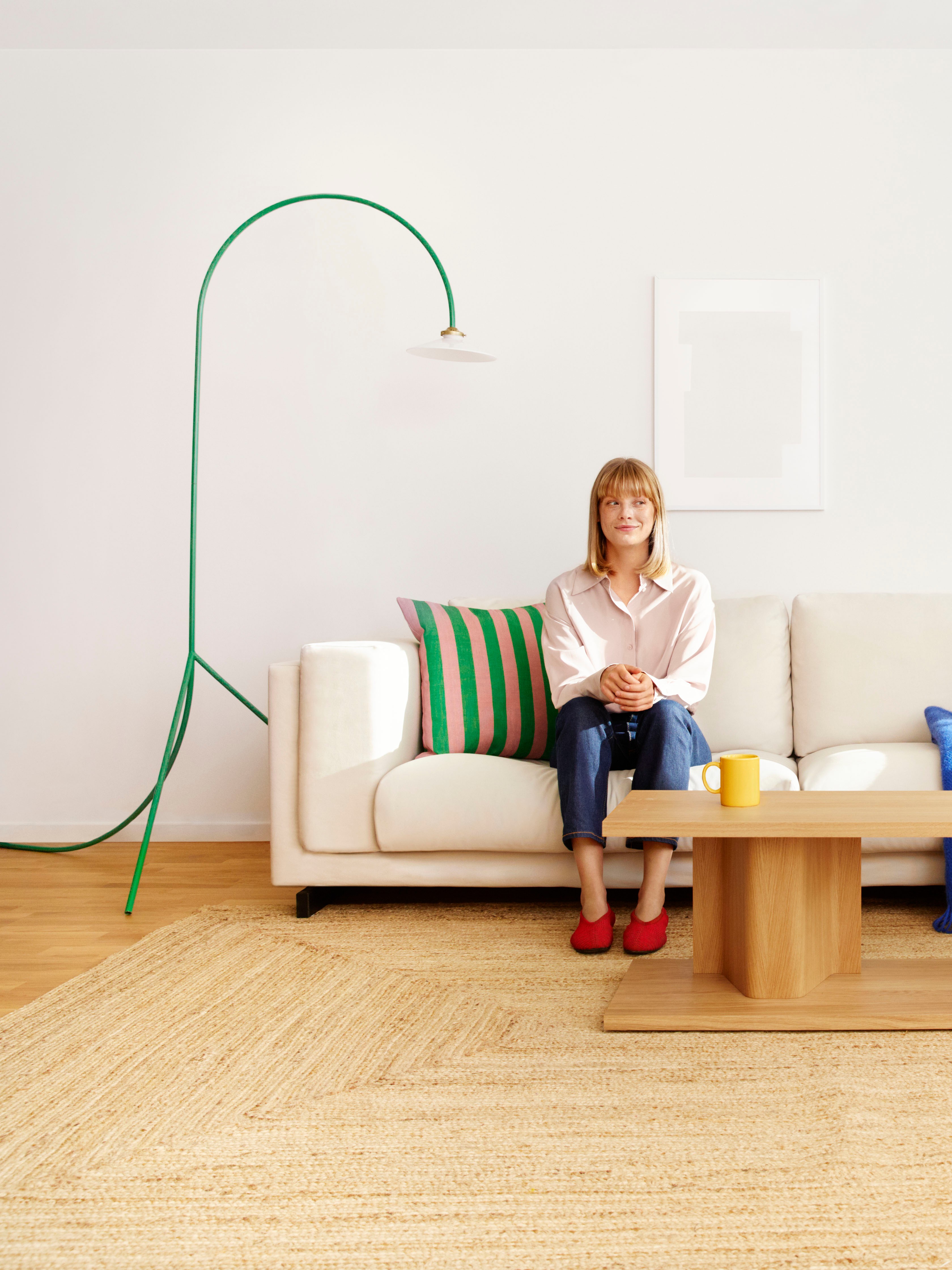 Woman sitting on a white sofa in a bright modern living room with wooden coffee table.