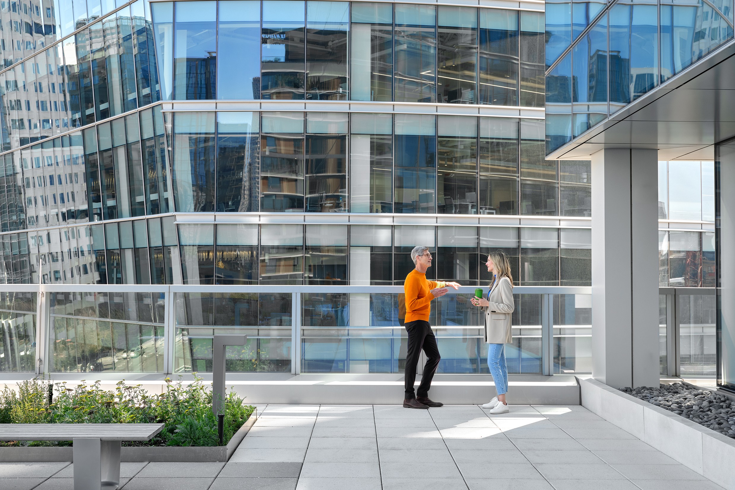 Professionals Networking on Modern Office Terrace Two people exchanging documents on a modern rooftop terrace with glass buildings in the background.